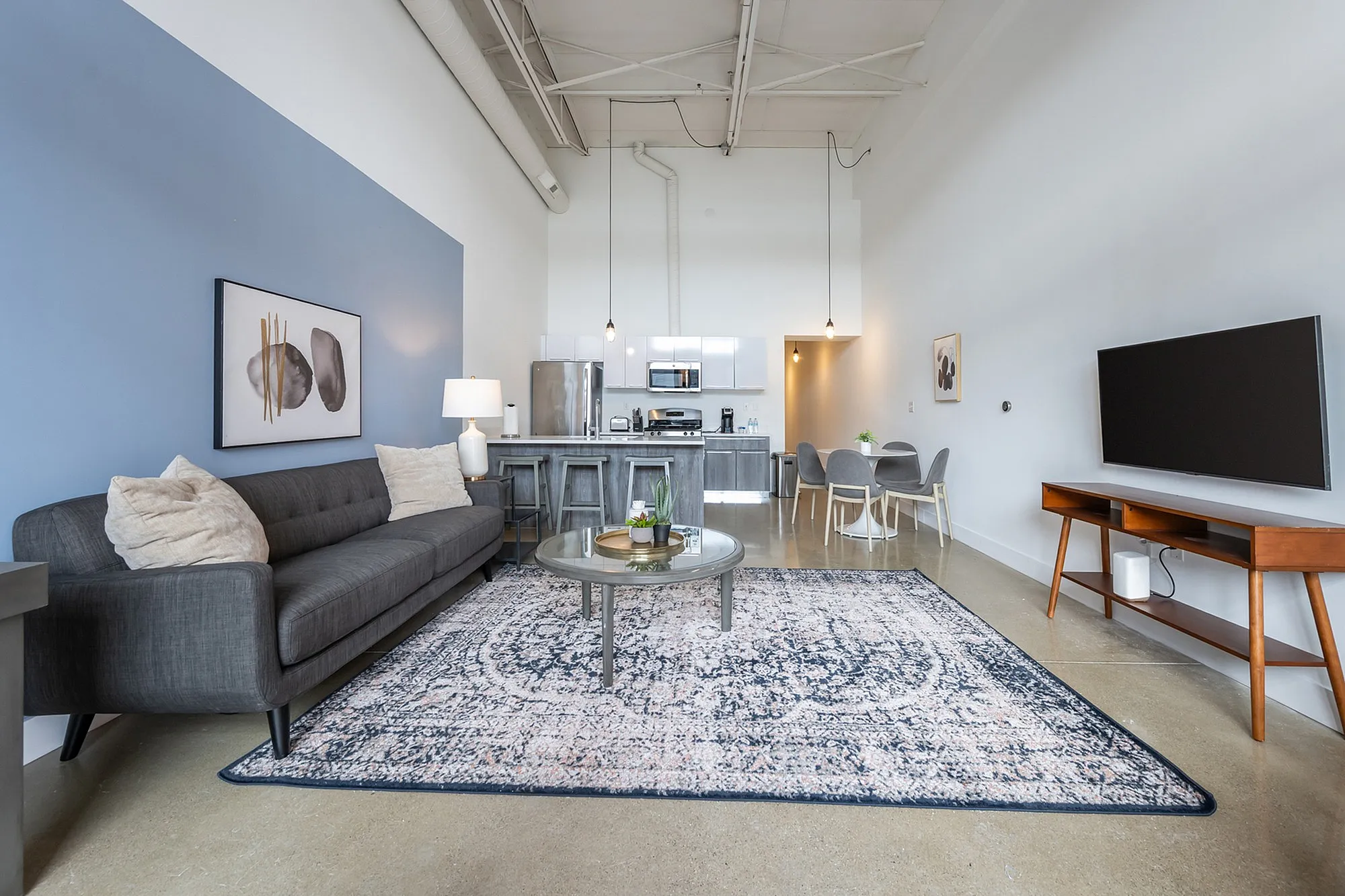 Modern open-plan living space with cozy gray sofa, chic blue accent wall, elegant dining area, and sleek contemporary kitchen.