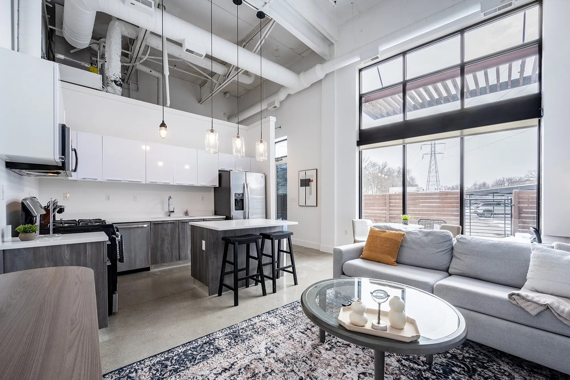 Modern loft-style apartment with high ceilings, large windows, and open-concept living area. Features a sleek kitchen with island seating and stylish pendant lighting.