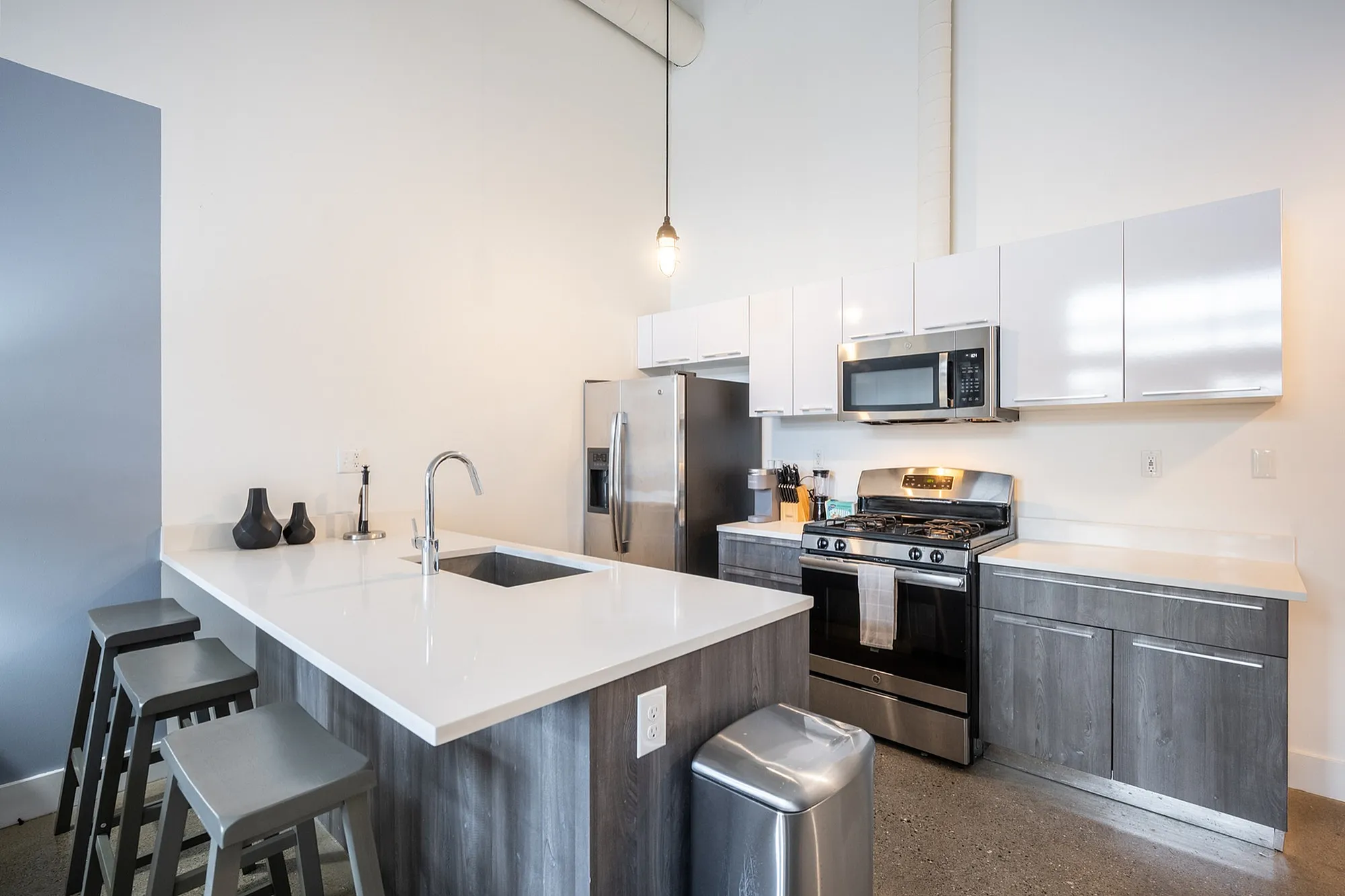 Modern apartment kitchen with sleek white countertops, stainless steel appliances, and elegant pendant lighting offering a sophisticated cooking space.