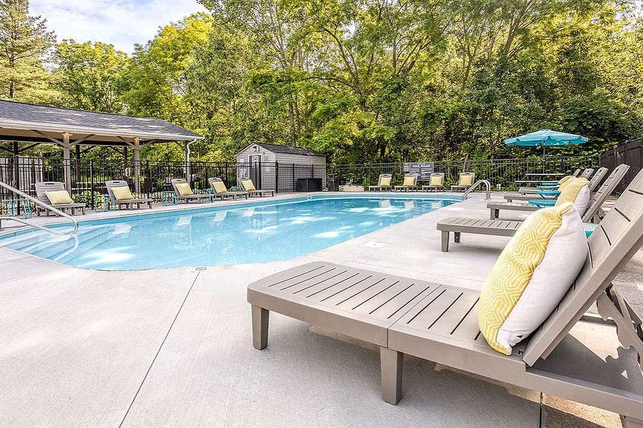 Inviting outdoor pool area with stylish lounge chairs, surrounded by lush greenery and shaded seating, perfect for relaxation and leisure.