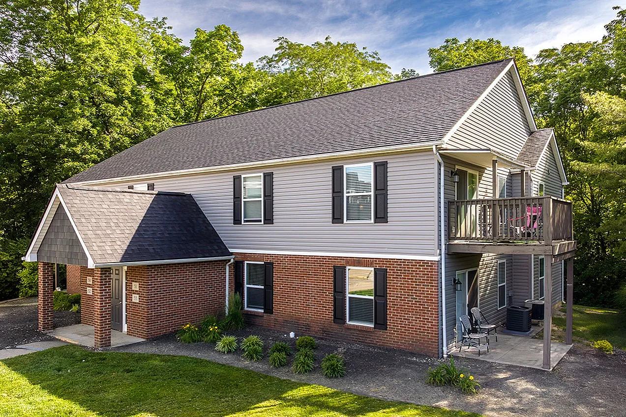 Charming two-story home with a brick facade and cozy balcony surrounded by lush greenery, perfect for serene living.