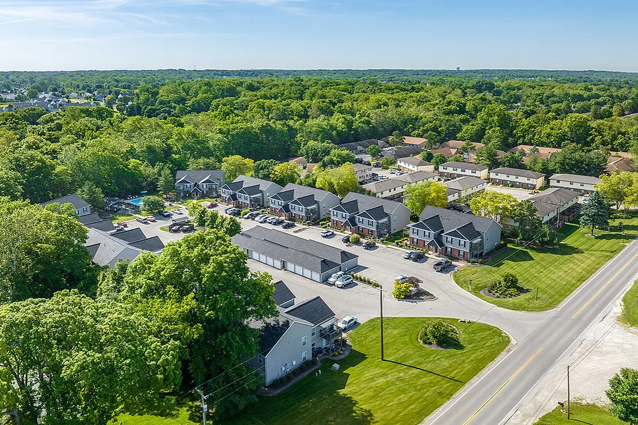 Charming aerial view of a serene apartment complex surrounded by lush greenery, featuring modern townhouses and ample parking.