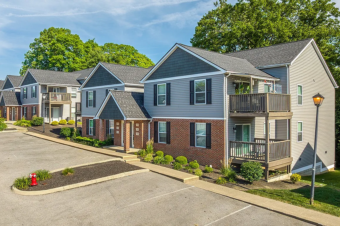 Charming residential apartment complex featuring modern two-story buildings with private balconies, surrounded by lush greenery and ample parking spaces.
