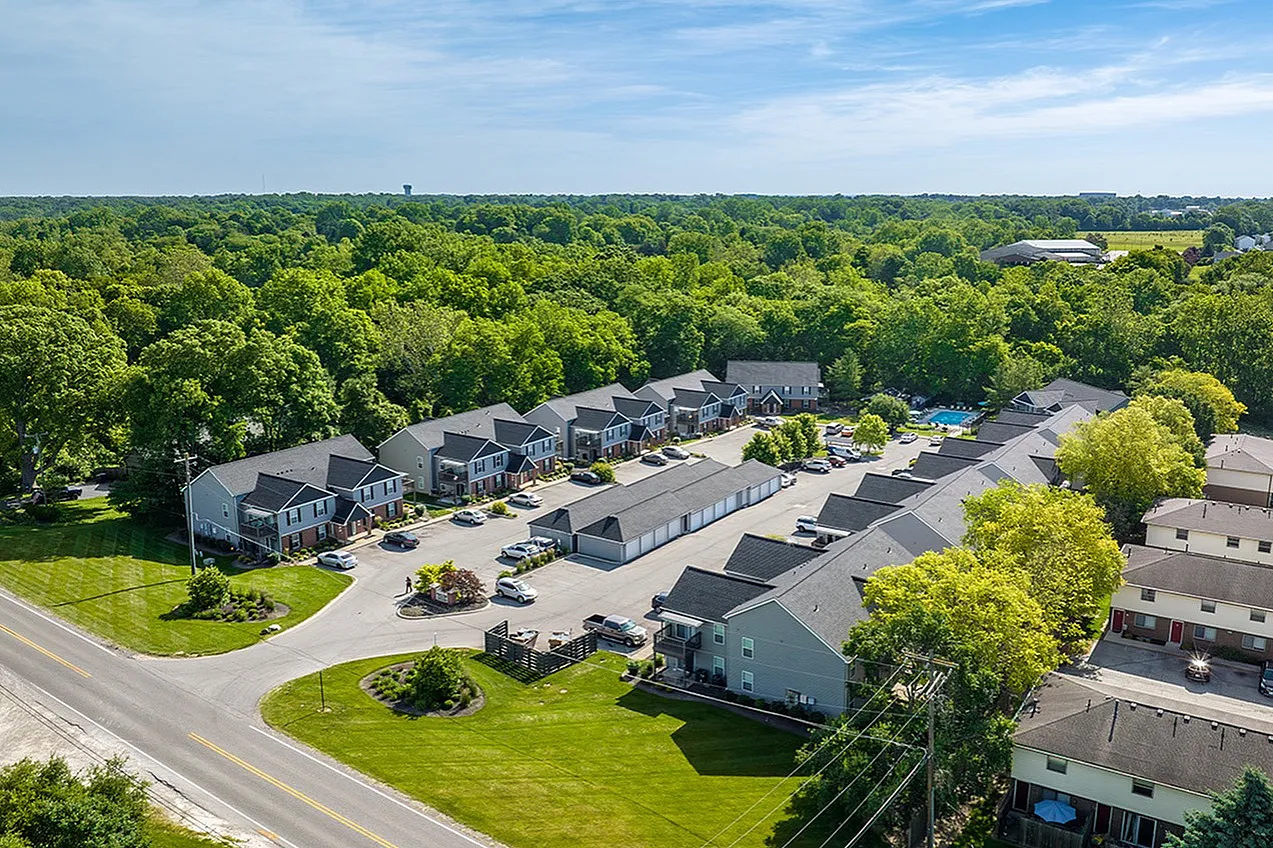 Charming aerial view of a serene residential community surrounded by lush greenery, showcasing modern townhouses and ample parking.