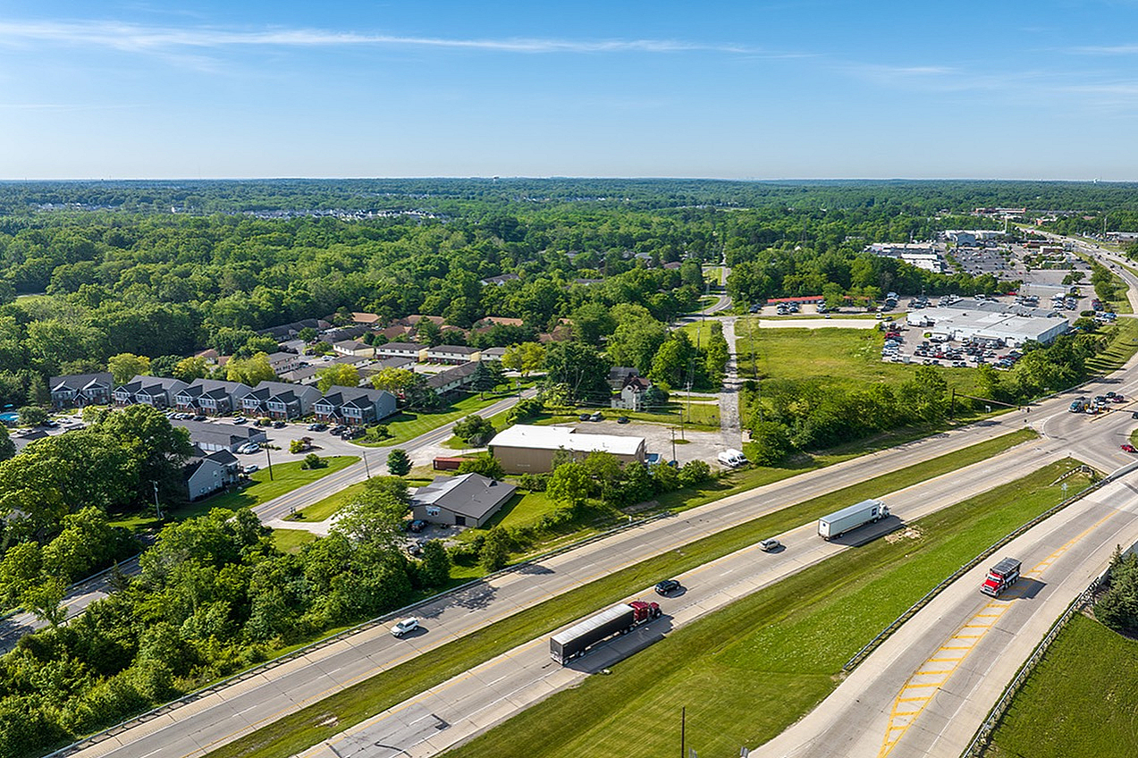 Aerial view of a serene neighborhood with lush greenery, modern homes, and nearby highway access for convenient transportation.