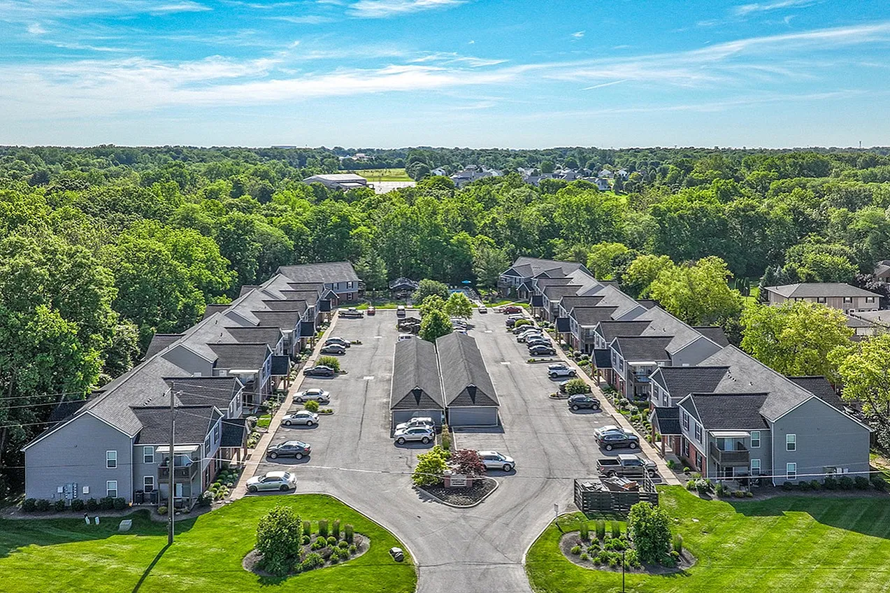 Aerial view of a serene apartment complex with lush greenery and ample parking, perfect for comfortable suburban living.