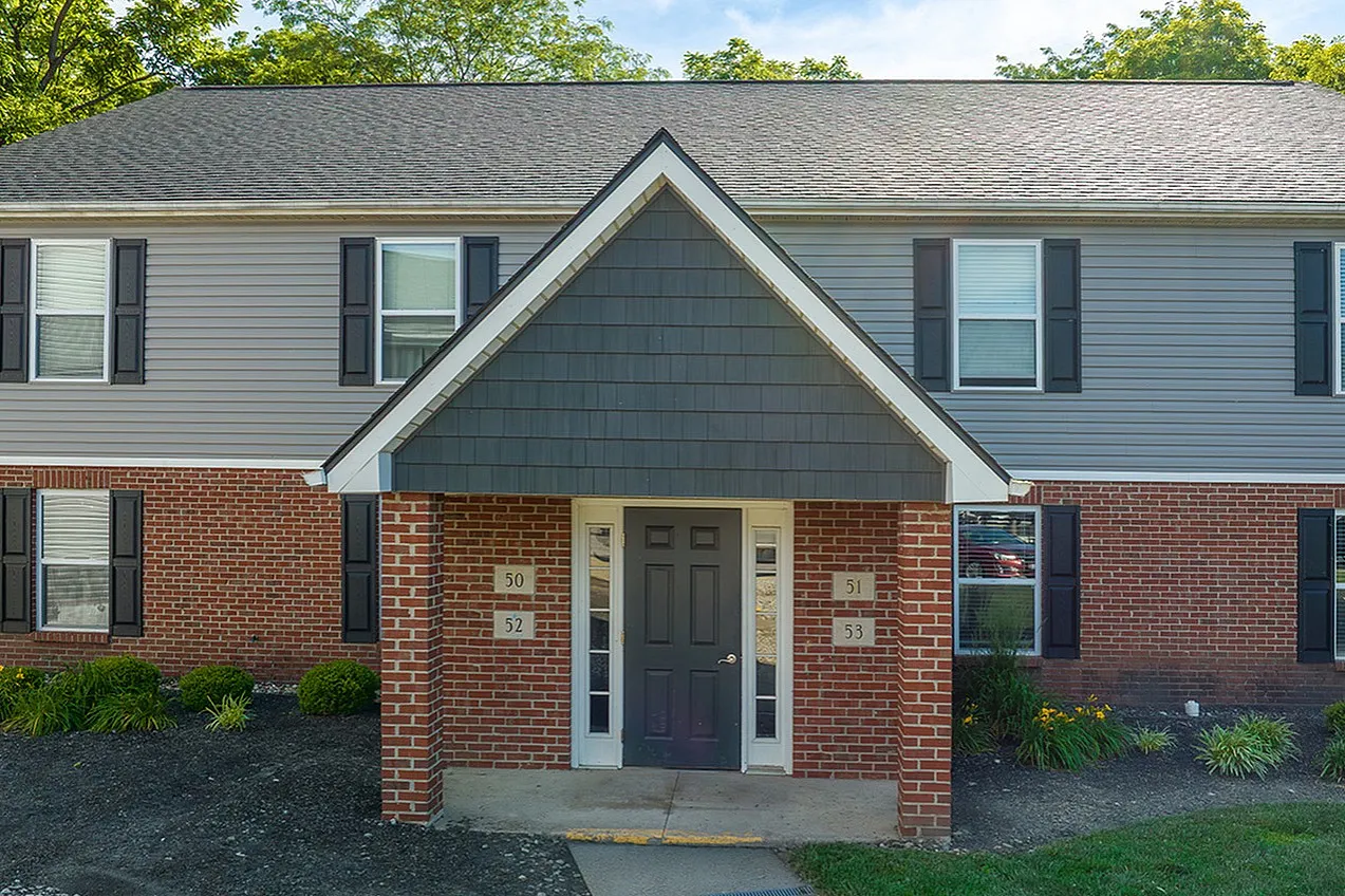 Charming two-story brick apartment building entrance with elegant landscaping and lush greenery, showcasing a welcoming and stylish exterior.