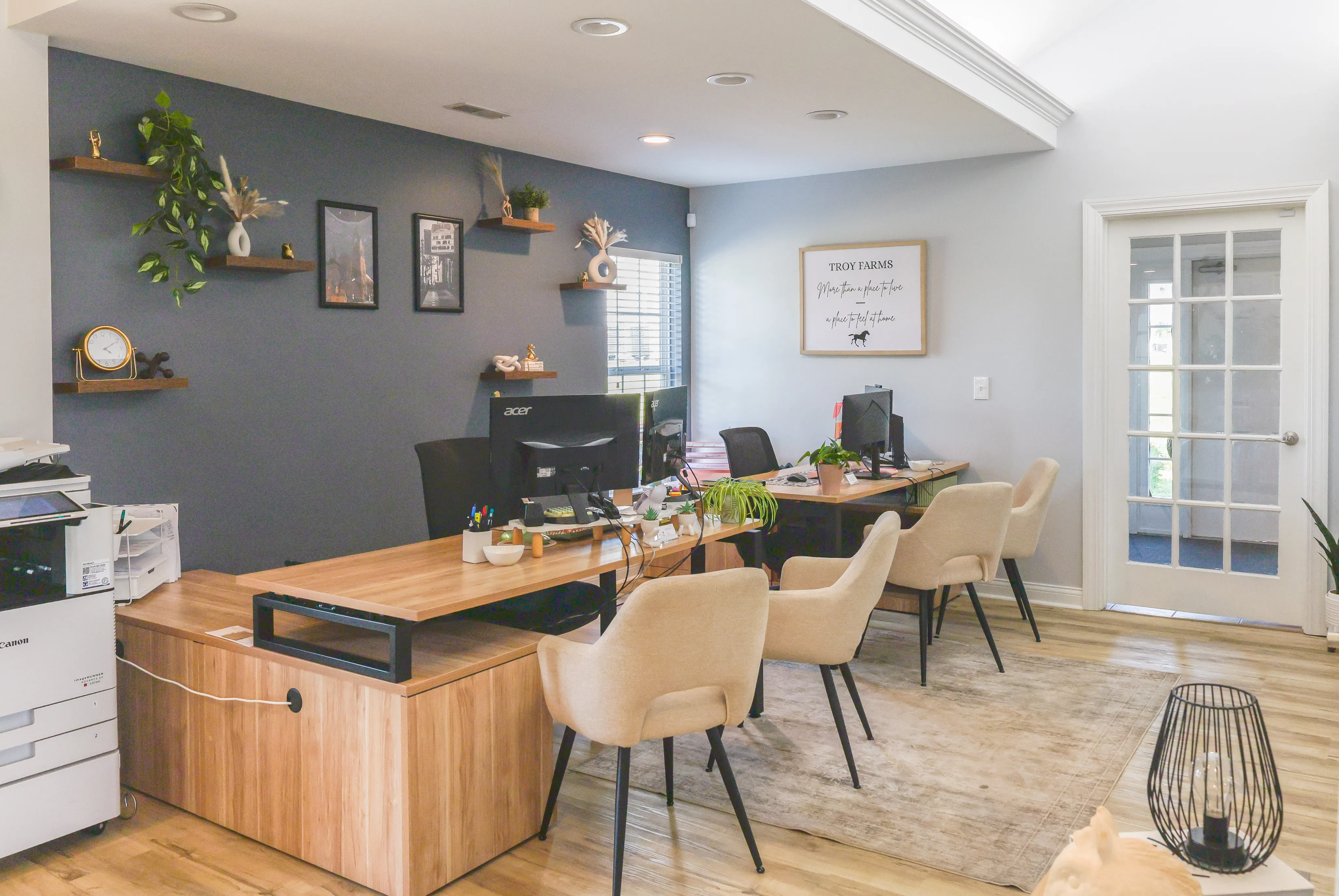 Modern office space with elegant decor, featuring a sleek wooden desk setup, stylish beige chairs, and vibrant wall art in a bright, inviting environment.