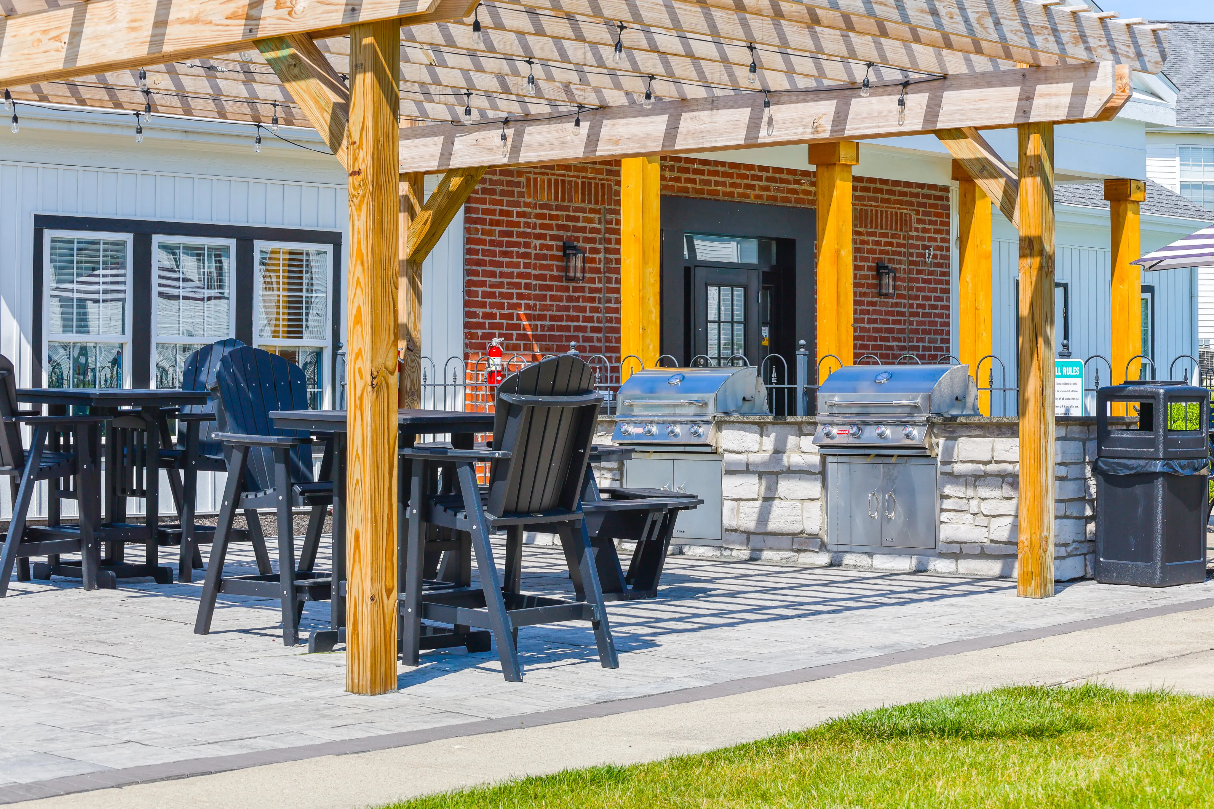 Charming outdoor patio featuring a rustic pergola, modern grills, and cozy seating area against a vibrant brick backdrop.