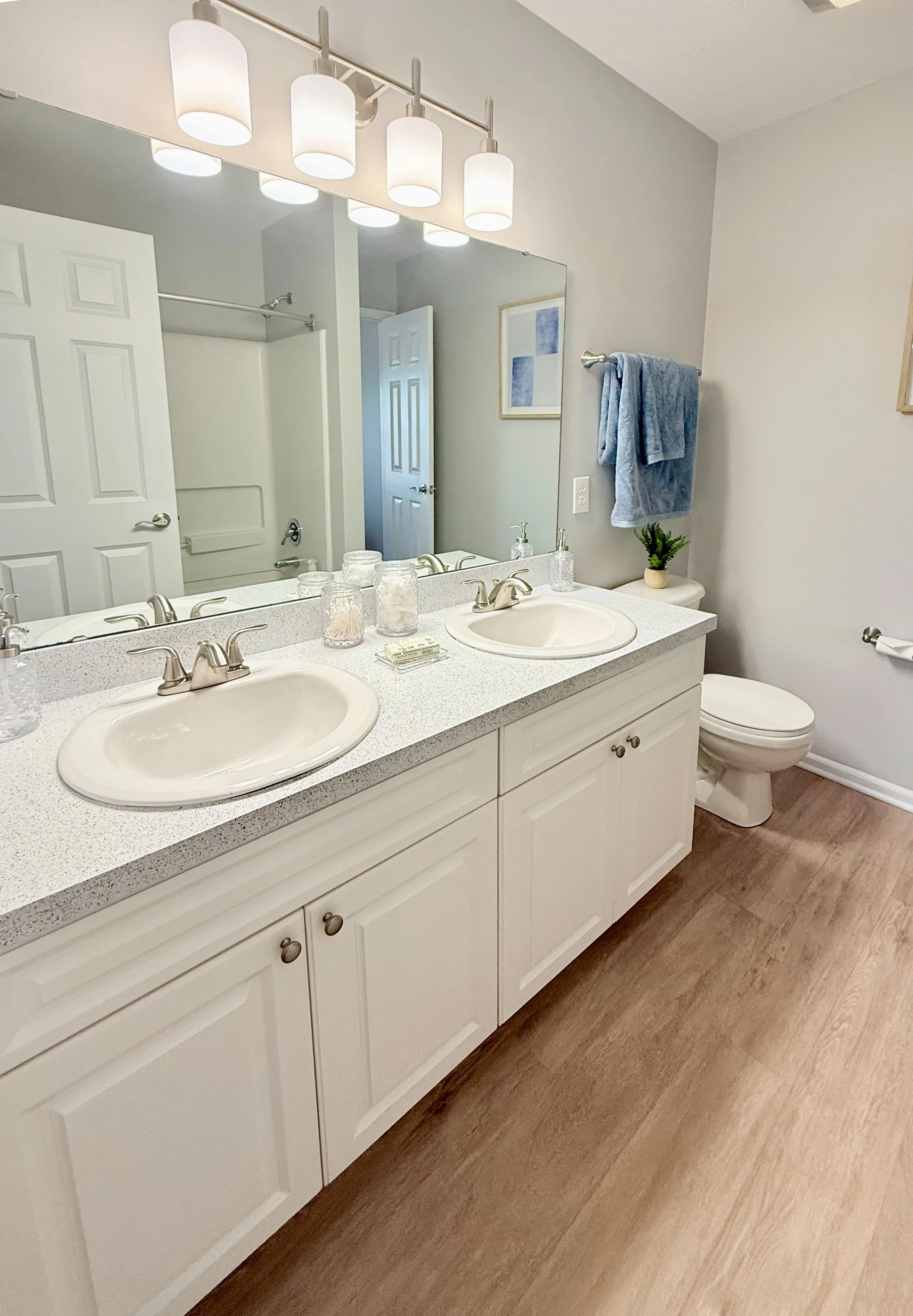Bright and modern bathroom with dual sinks, elegant quartz countertops, and warm wood flooring.