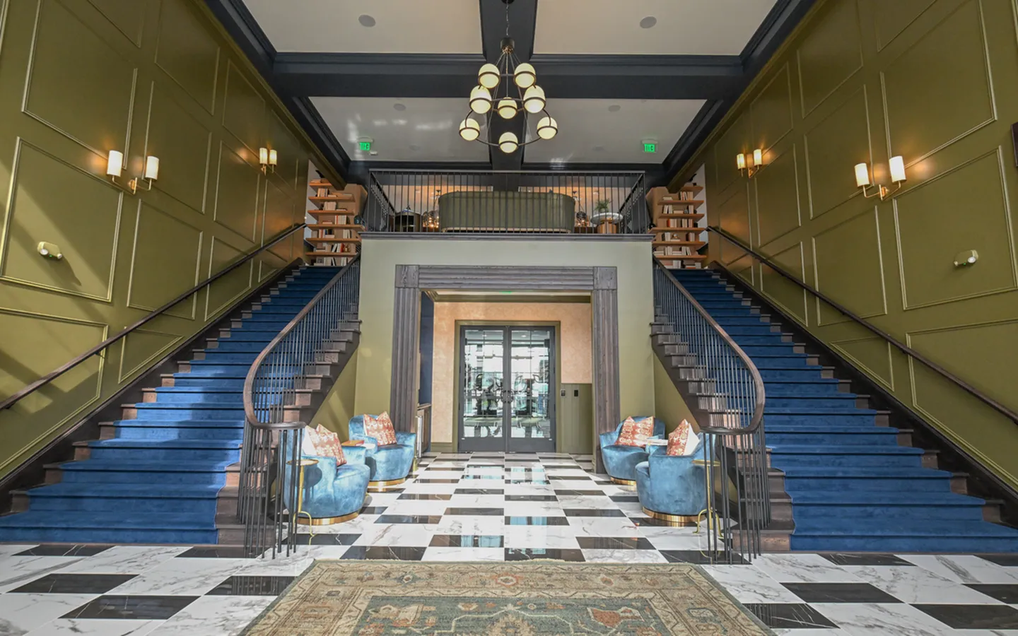 Elegant lobby with dual grand staircases, plush seating, and modern chandelier in a luxurious apartment building.