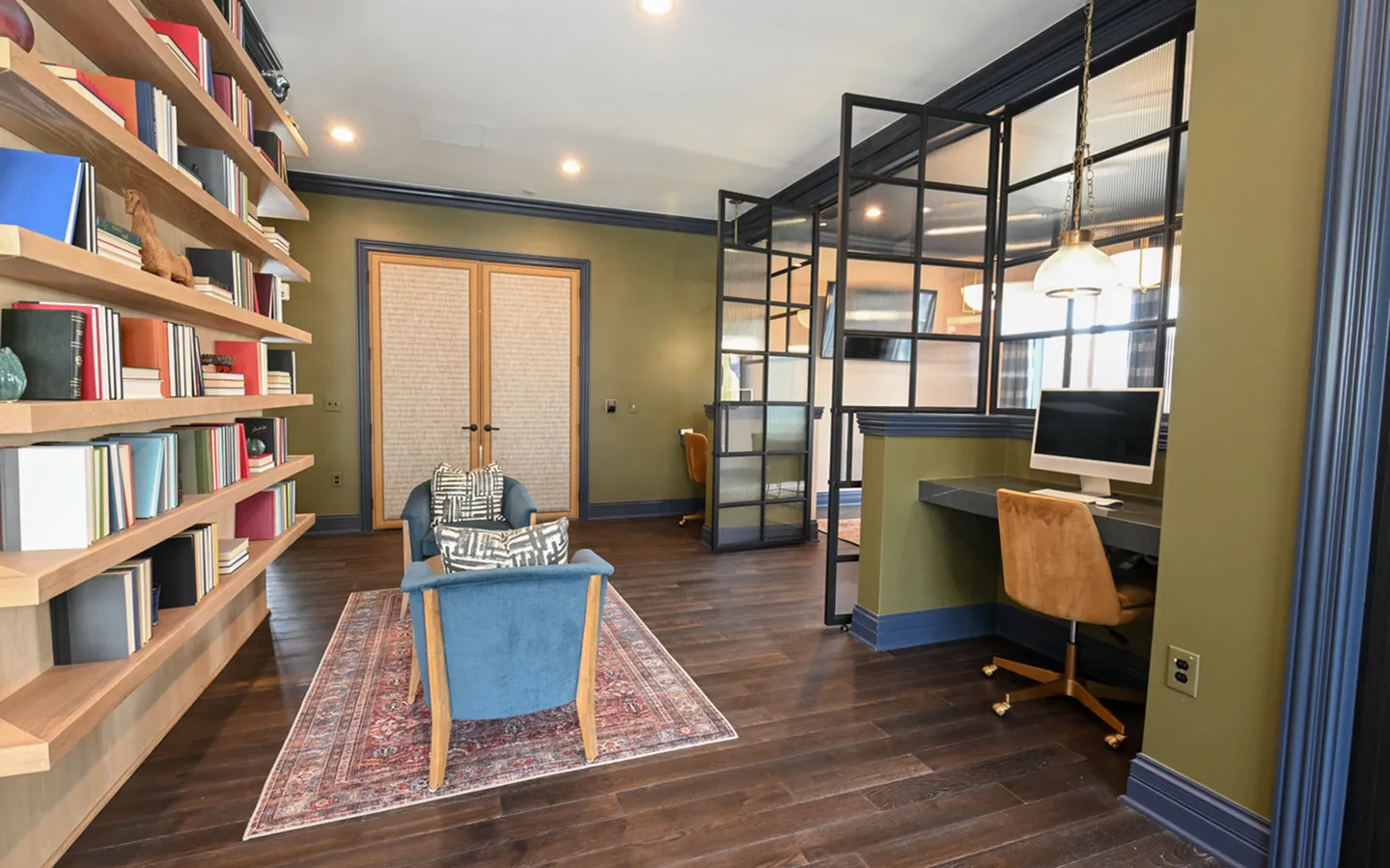 Chic home office with cozy reading nook, elegant bookshelves, rich wood flooring, and modern glass partitions creating a sophisticated ambiance.