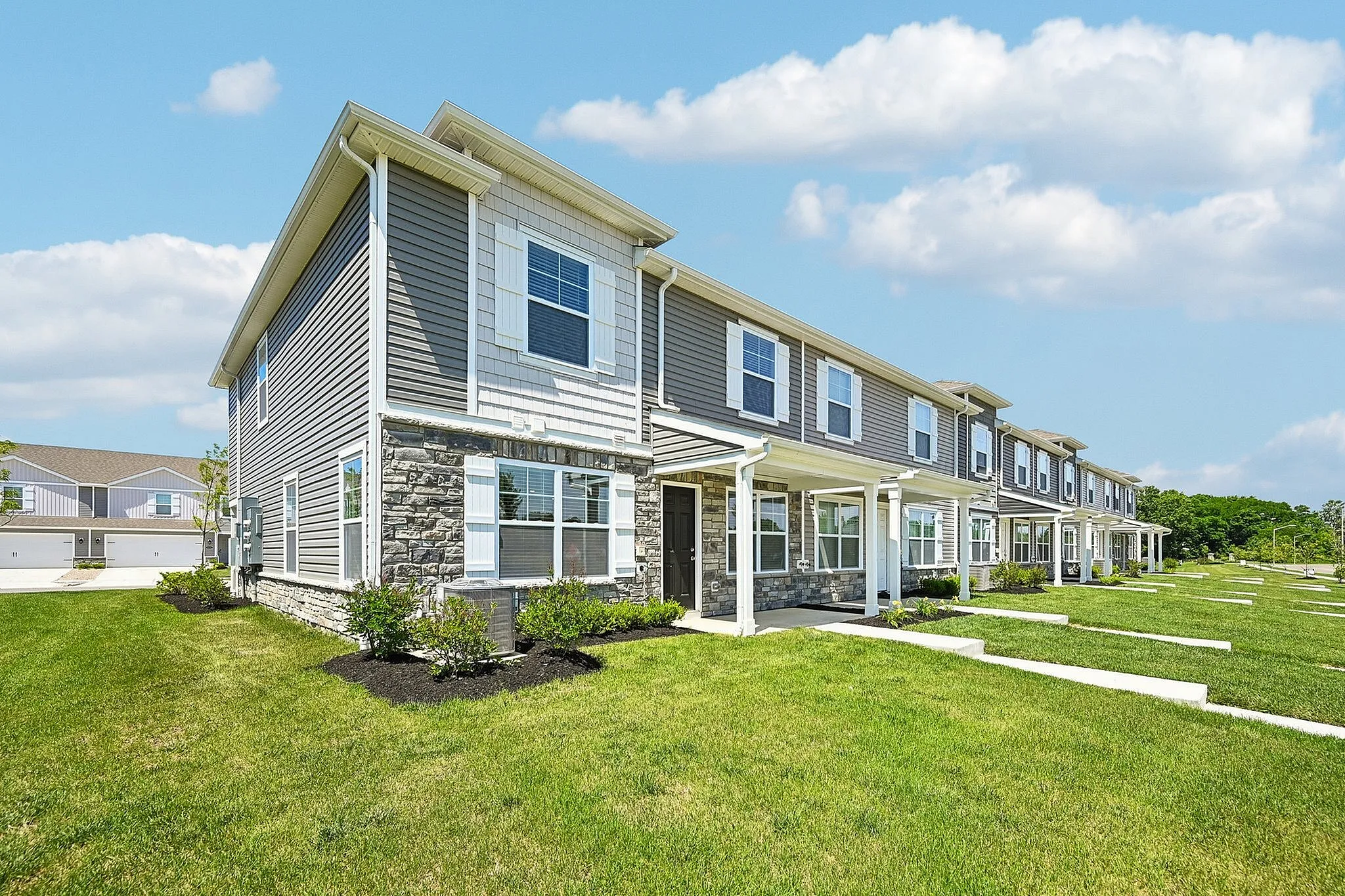 Charming row of modern townhouses with well-maintained lawns, showcasing elegant architecture under a bright blue sky.
