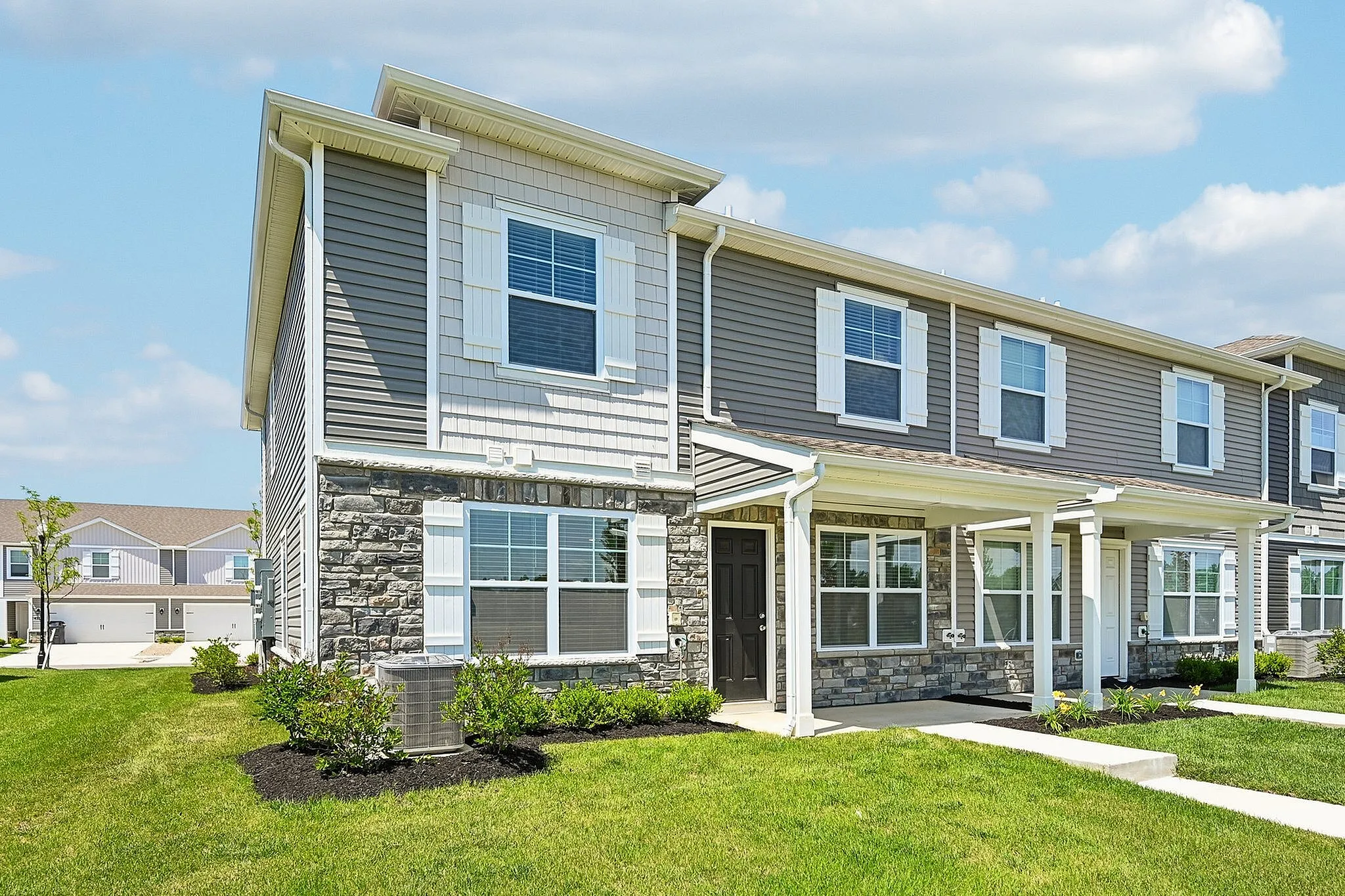 Charming two-story townhouse with modern design, stone facade, and lush green lawn under a clear blue sky.