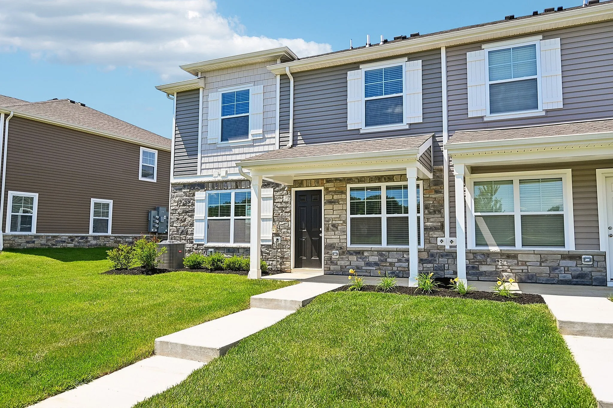 Charming townhouse with modern stone facade and lush green lawn, perfect for family living.