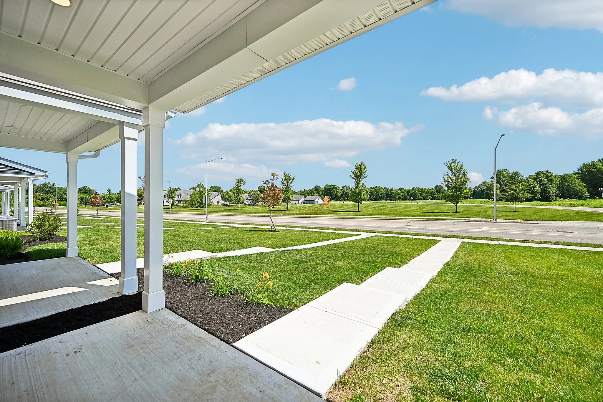 Inviting front porch with landscaped gardens overlooking a scenic green expanse and a quiet street, perfect for relaxation.