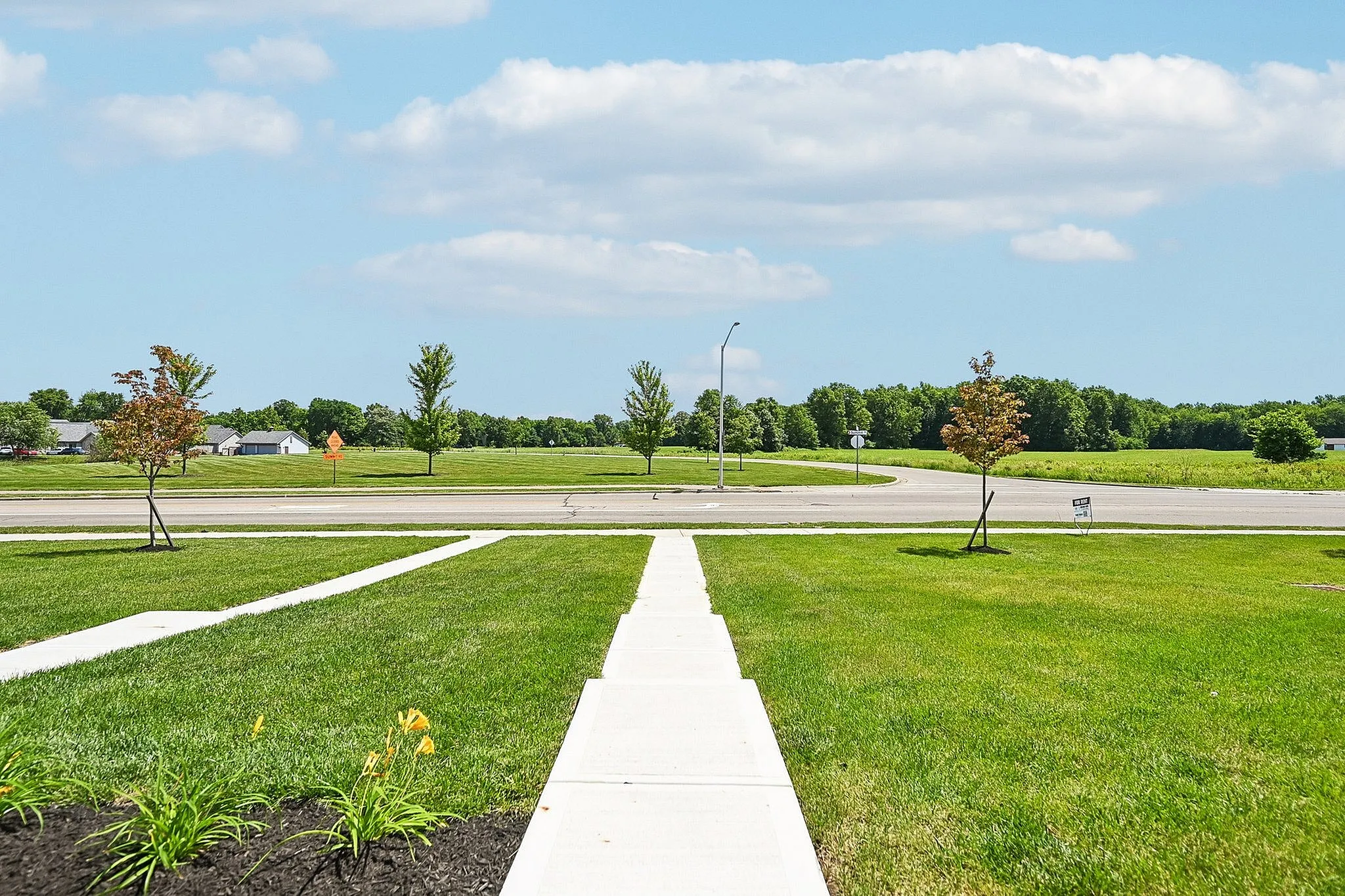 Inviting view from a fresh, green lawn overlooking a wide, open field with vibrant blue skies and fluffy clouds.
