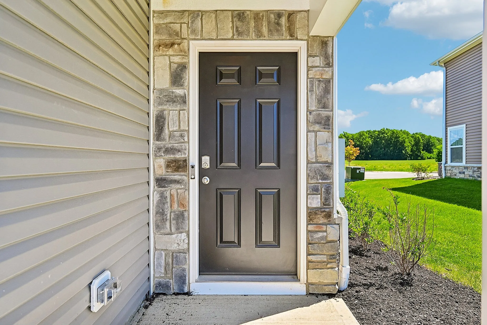 Inviting entrance with a sleek black door surrounded by elegant stonework, leading to a welcoming home in a tranquil neighborhood.