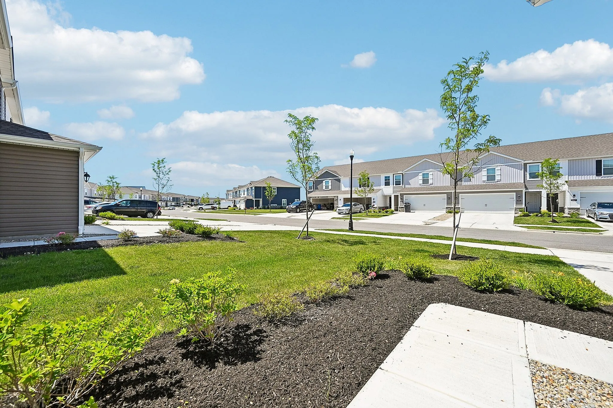Charming suburban neighborhood view showcasing modern townhouses, manicured lawns, and a bright blue sky.