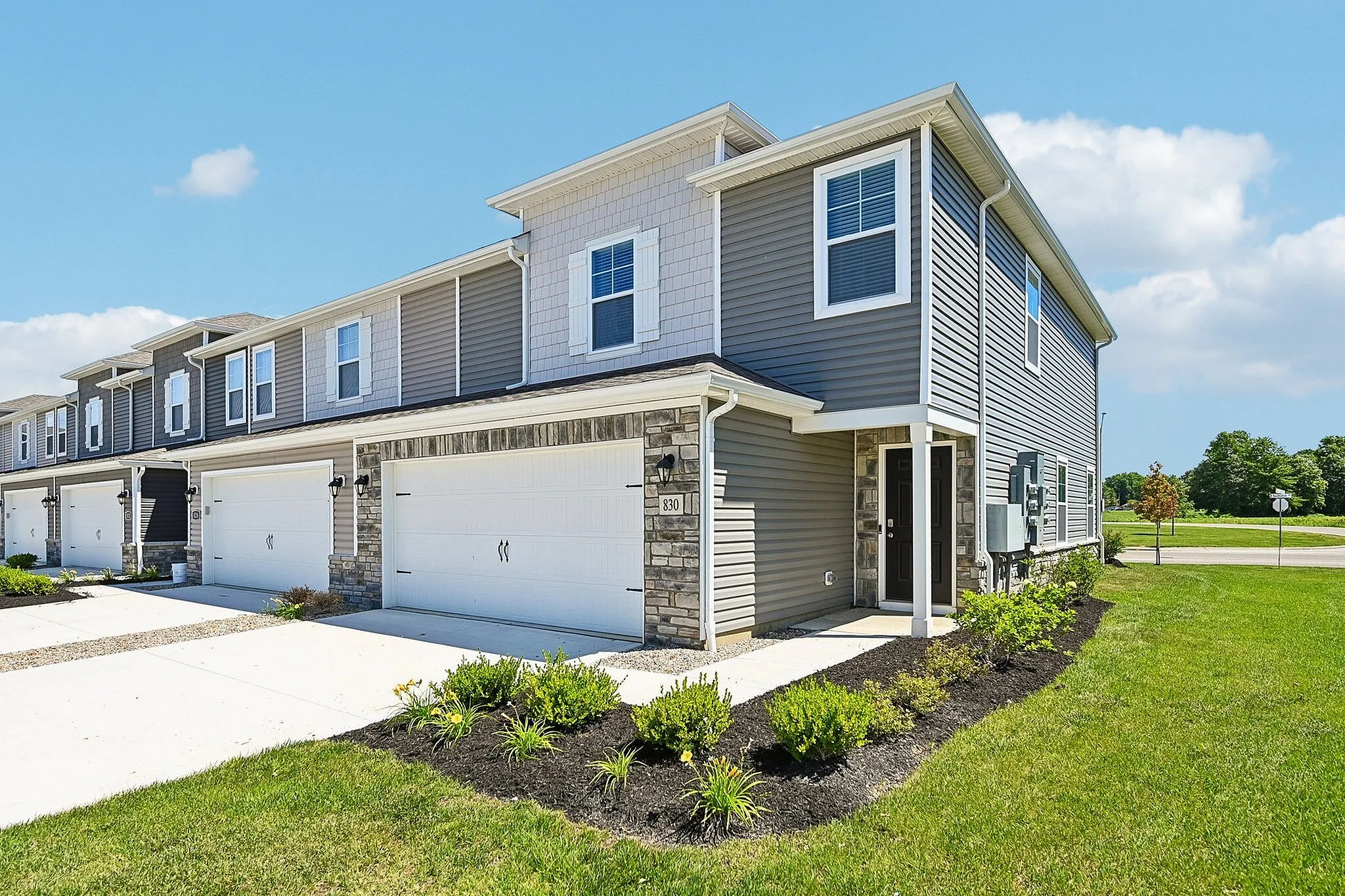 Elegant townhouse with modern siding and stone accents, featuring double garage and well-maintained front garden under a clear blue sky.