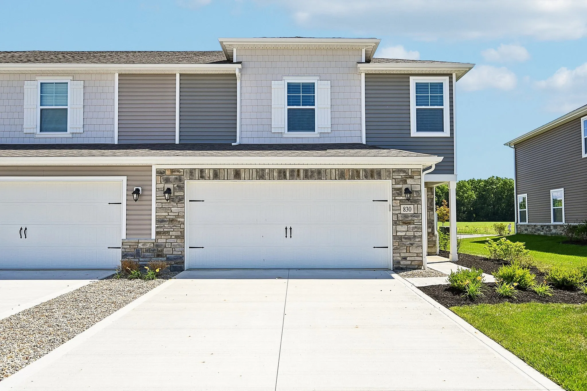 Charming suburban duplex with a modern facade, featuring a spacious two-car garage and well-manicured front lawn.