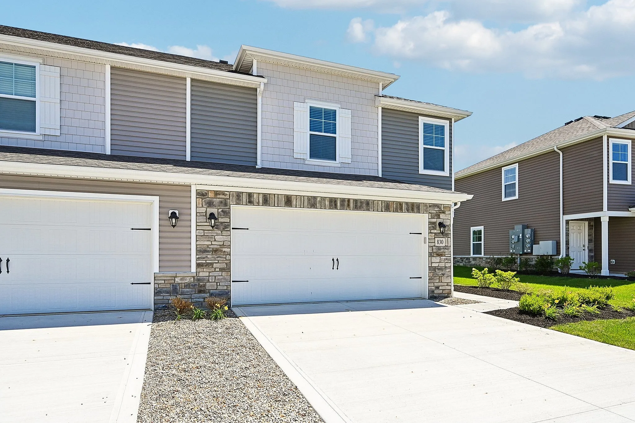 Modern townhouse exterior with a double garage, sleek siding, and stone accents, set in a sunny and vibrant neighborhood.