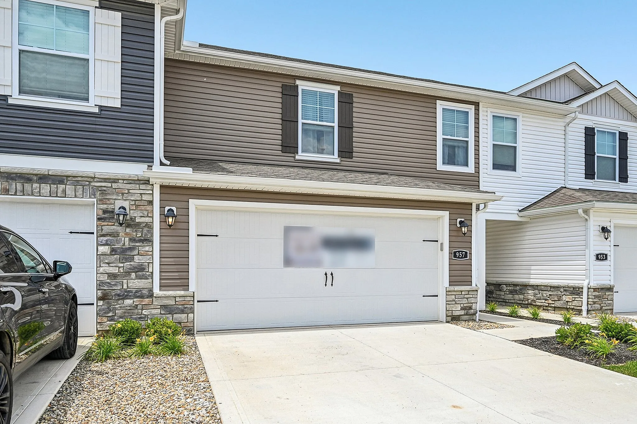 Charming two-story townhouse with elegant stone accents, featuring a spacious two-car garage and modern exterior design.