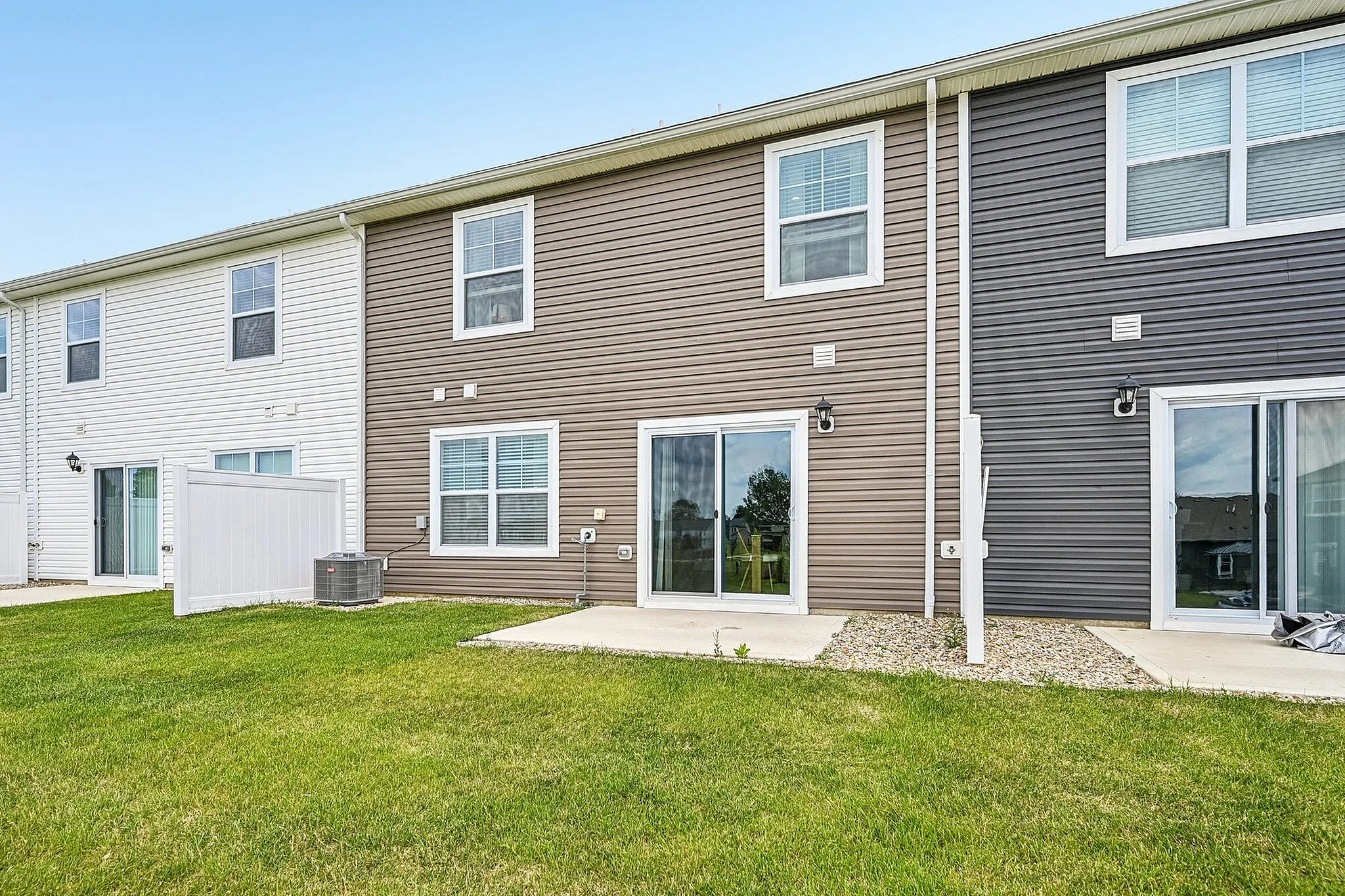 Charming townhouse with modern siding, lush green lawn, large windows, and inviting patio doors for a bright living experience.