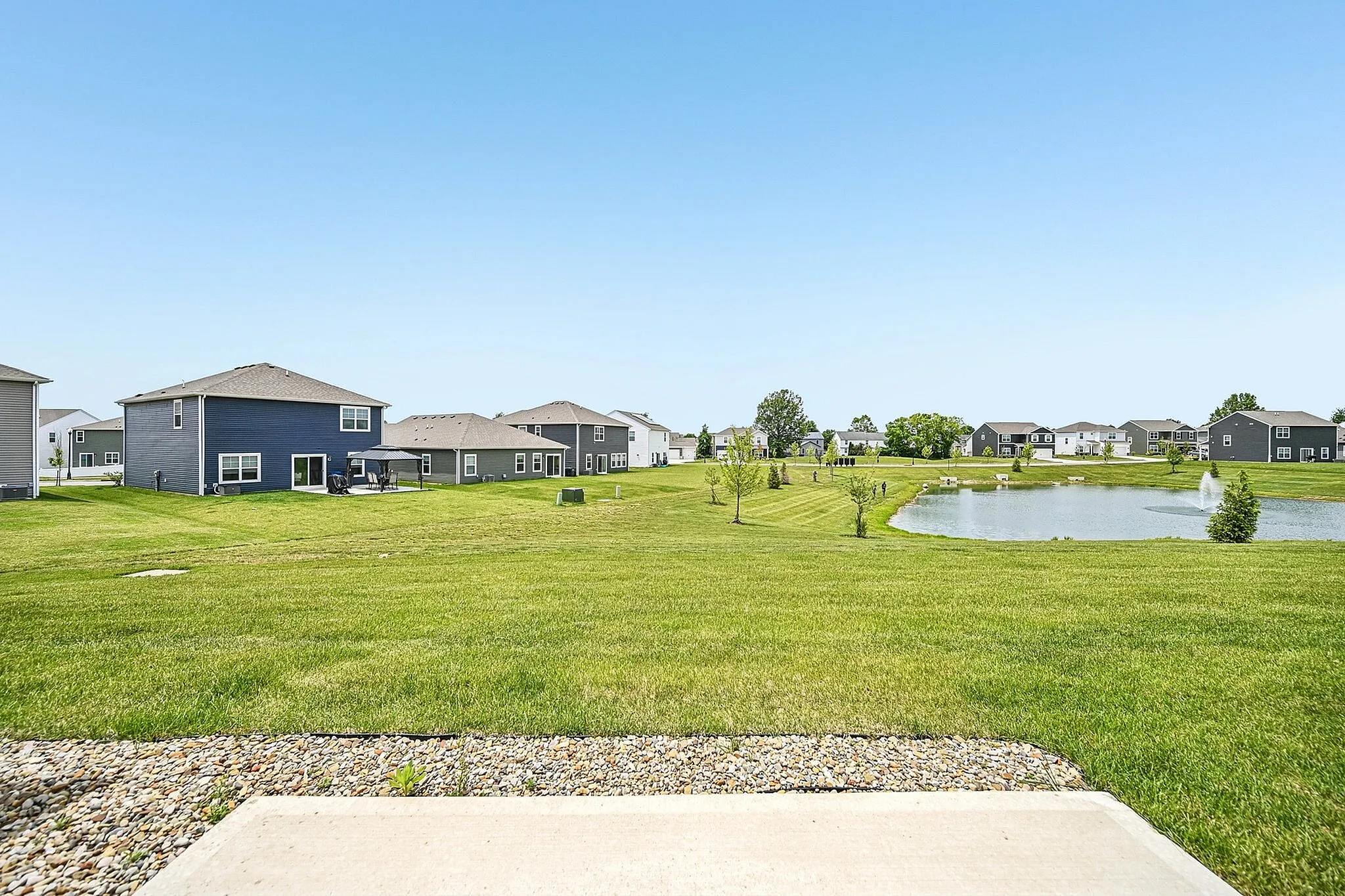 Charming suburban neighborhood with modern homes overlooking a serene pond and lush green lawns, offering a peaceful and inviting community setting.
