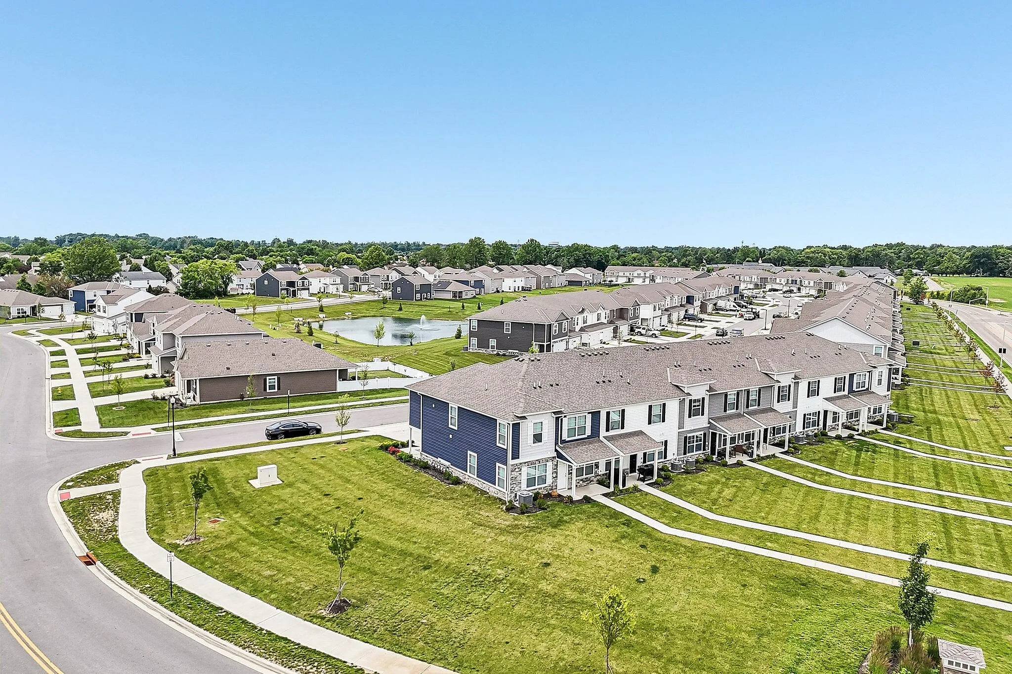 Peaceful suburban neighborhood with charming townhouses, lush green lawns, and a scenic pond featuring a fountain.