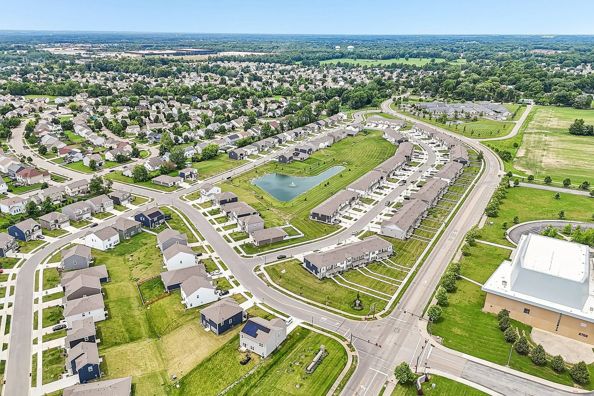 Charming suburban neighborhood aerial view showcasing well-planned streets, modern homes, and lush green spaces with a central pond.