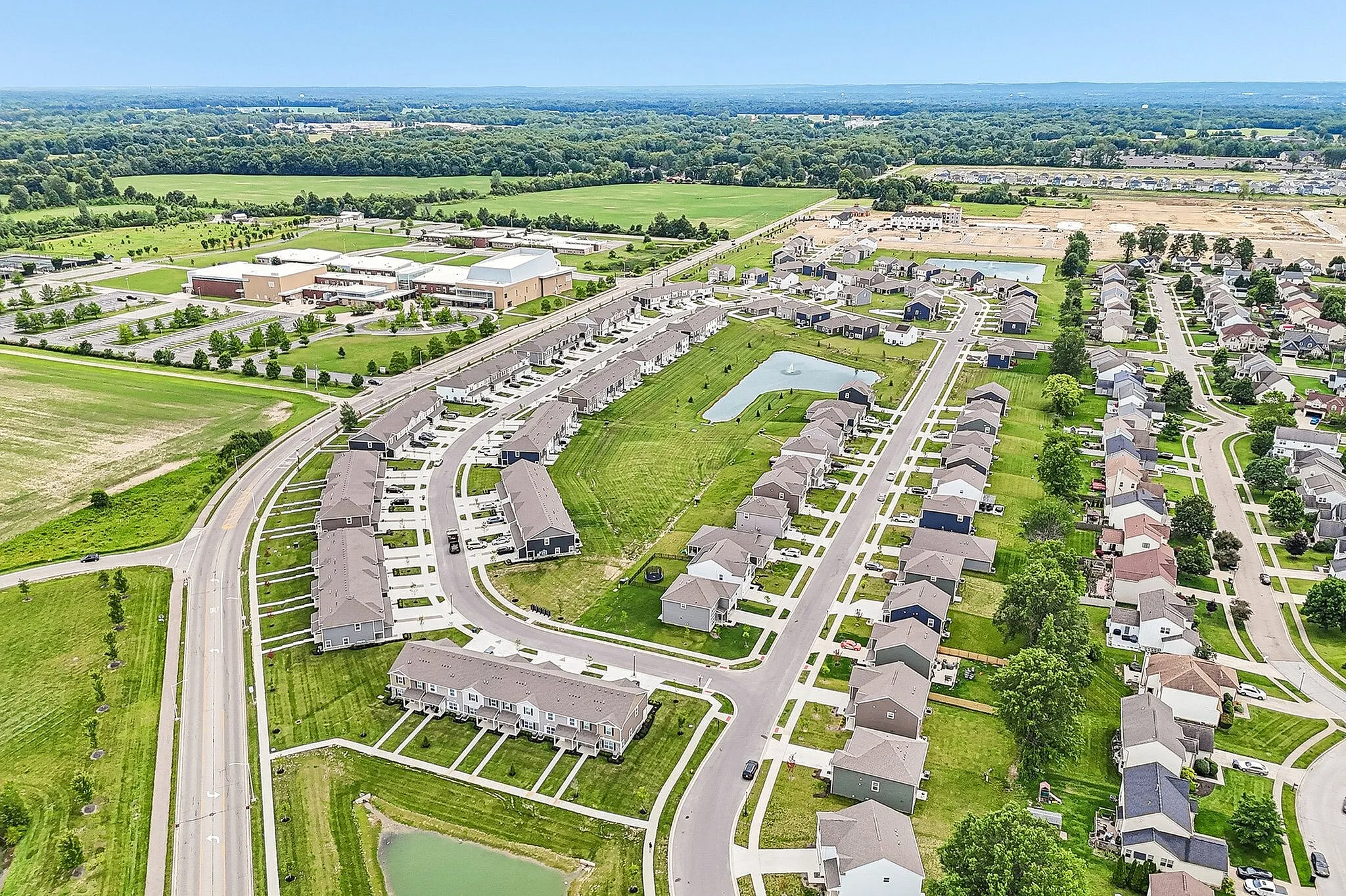 Charming aerial view of a vibrant suburban neighborhood with modern homes, lush green lawns, and a serene decorative pond, ideal for family living.