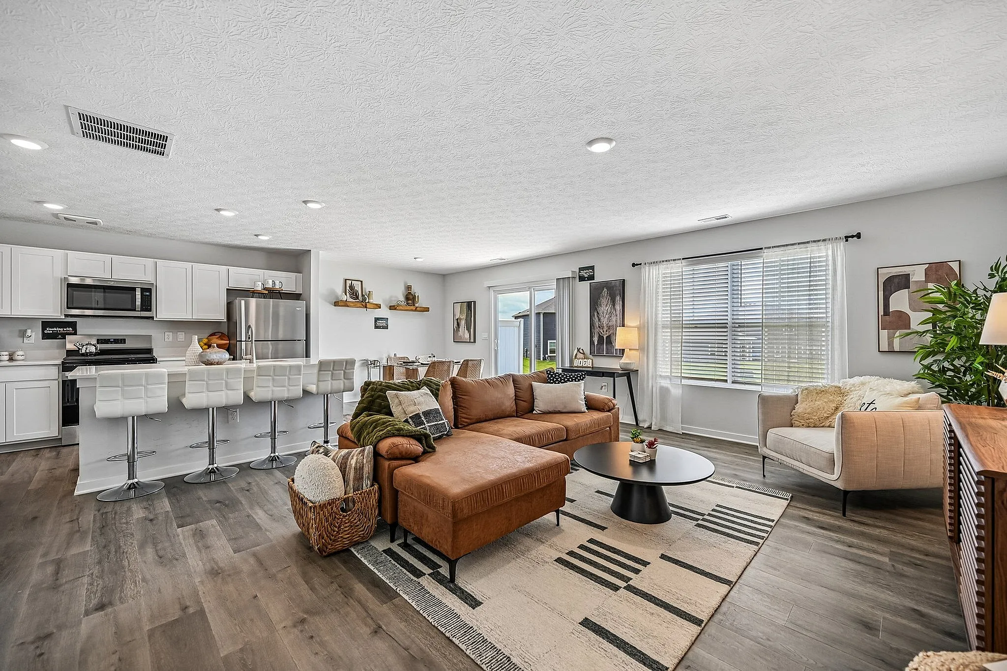 Modern open-concept living space featuring a stylish kitchen with white cabinetry, cozy brown sofa, and inviting dining area, perfect for entertaining and relaxation.
