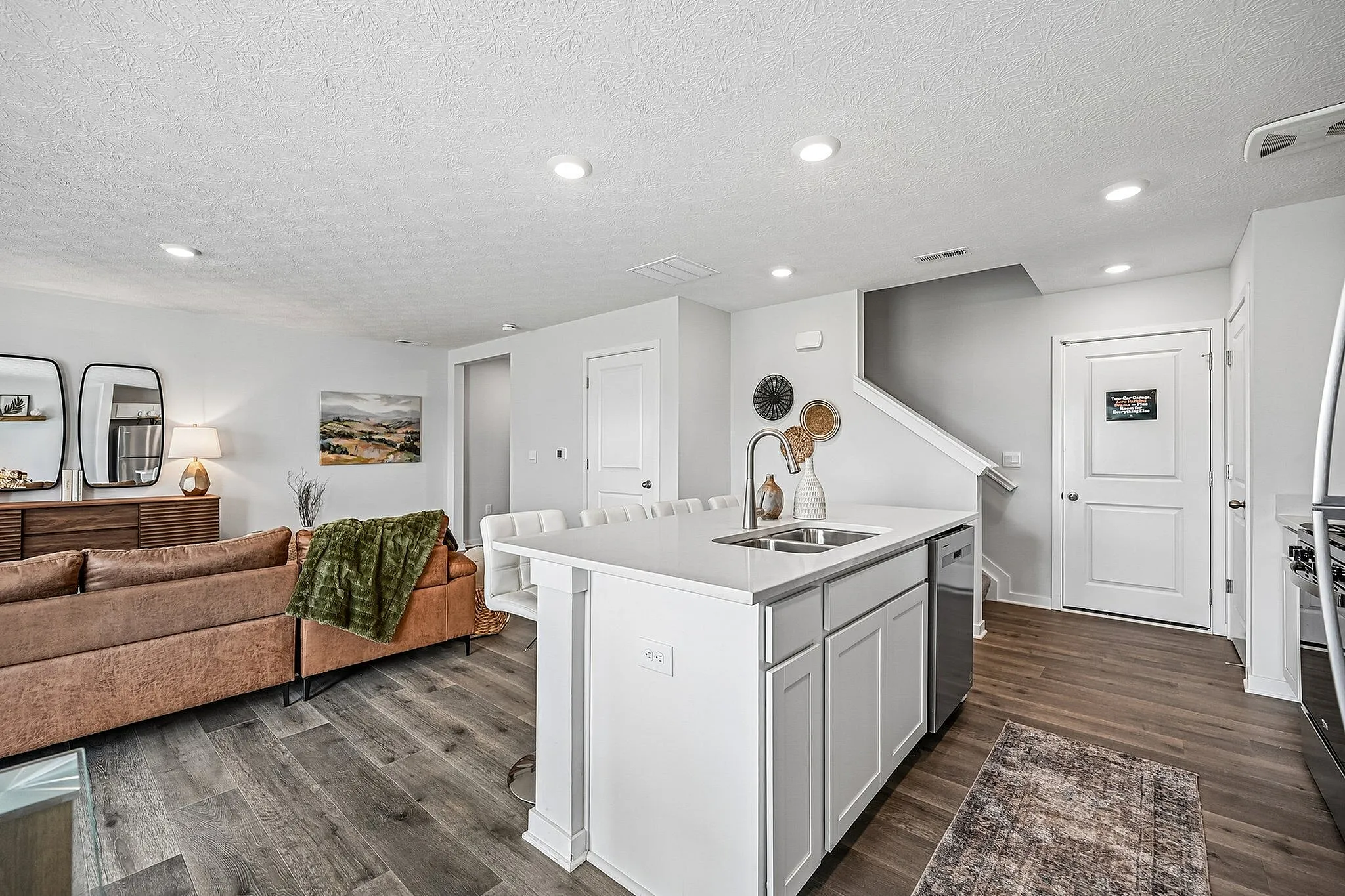Chic open-concept living area features a modern kitchen with island, cozy living room with stylish decor, and elegant hardwood floors.