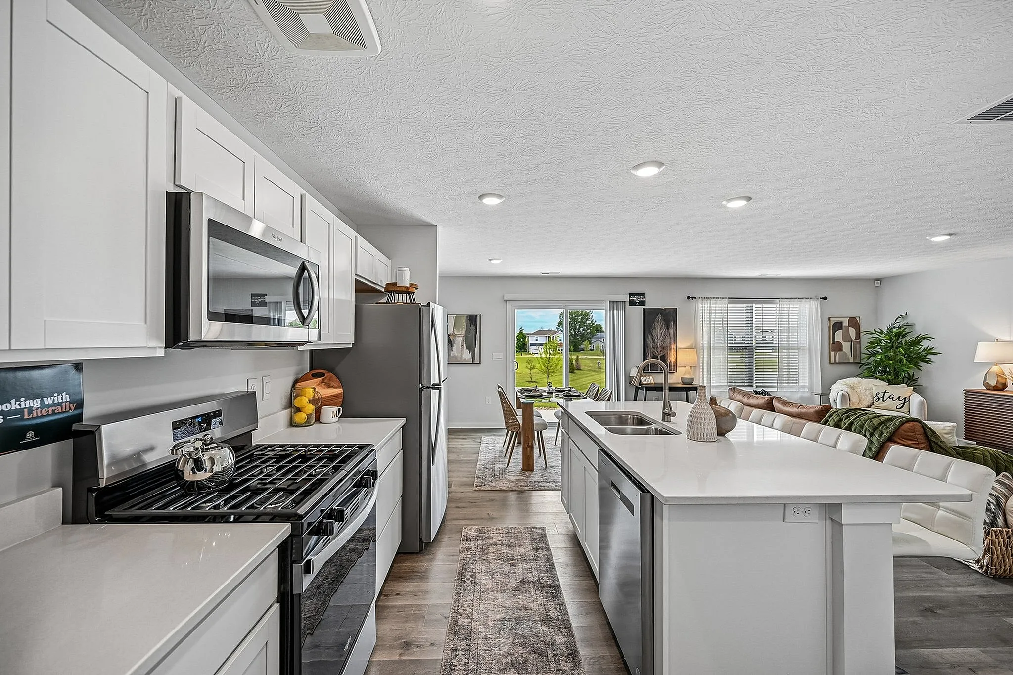 Modern open-concept kitchen and living area with sleek white cabinets, stainless steel appliances, and a bright, airy ambiance overlooking a scenic backyard view.