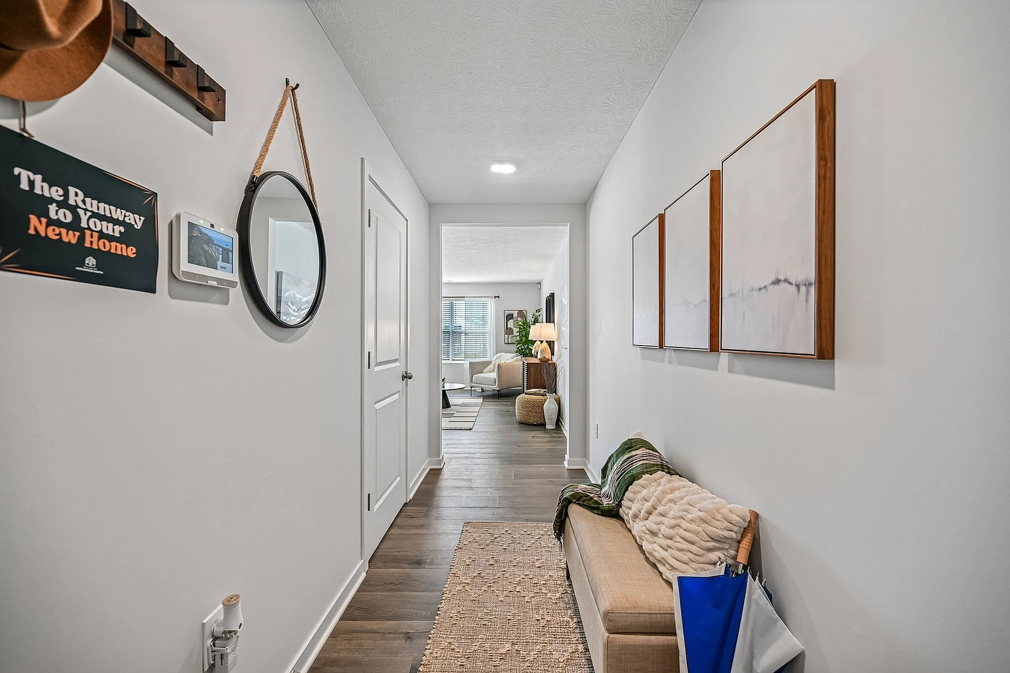 Welcoming apartment hallway featuring stylish decor, mirror, wall art, and cozy seating leading to a bright living room.