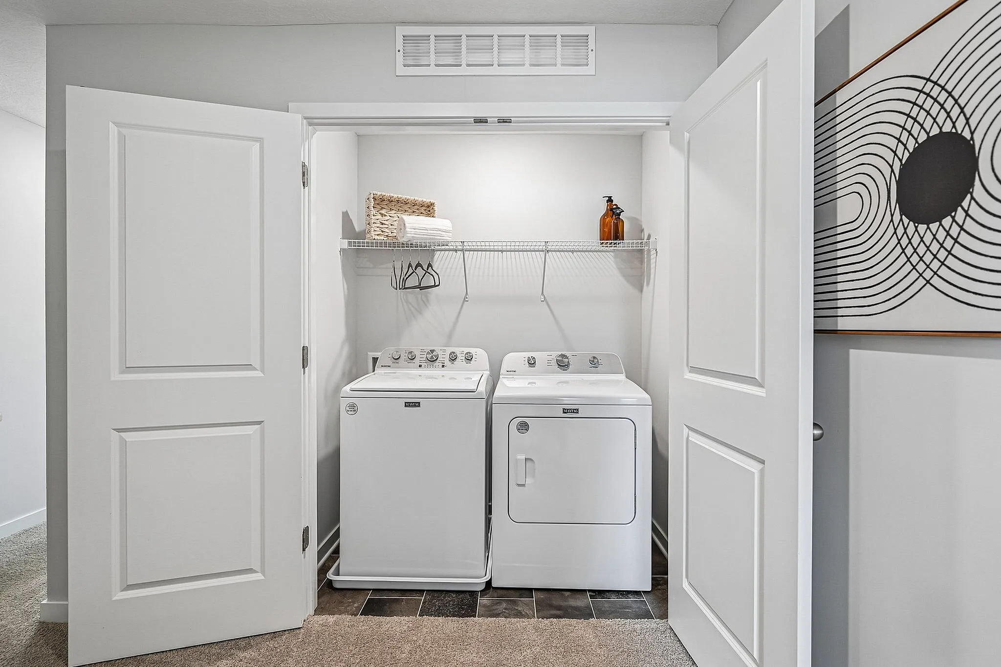 Modern laundry nook with sleek washer and dryer, accented by stylish shelving and artistic decor.