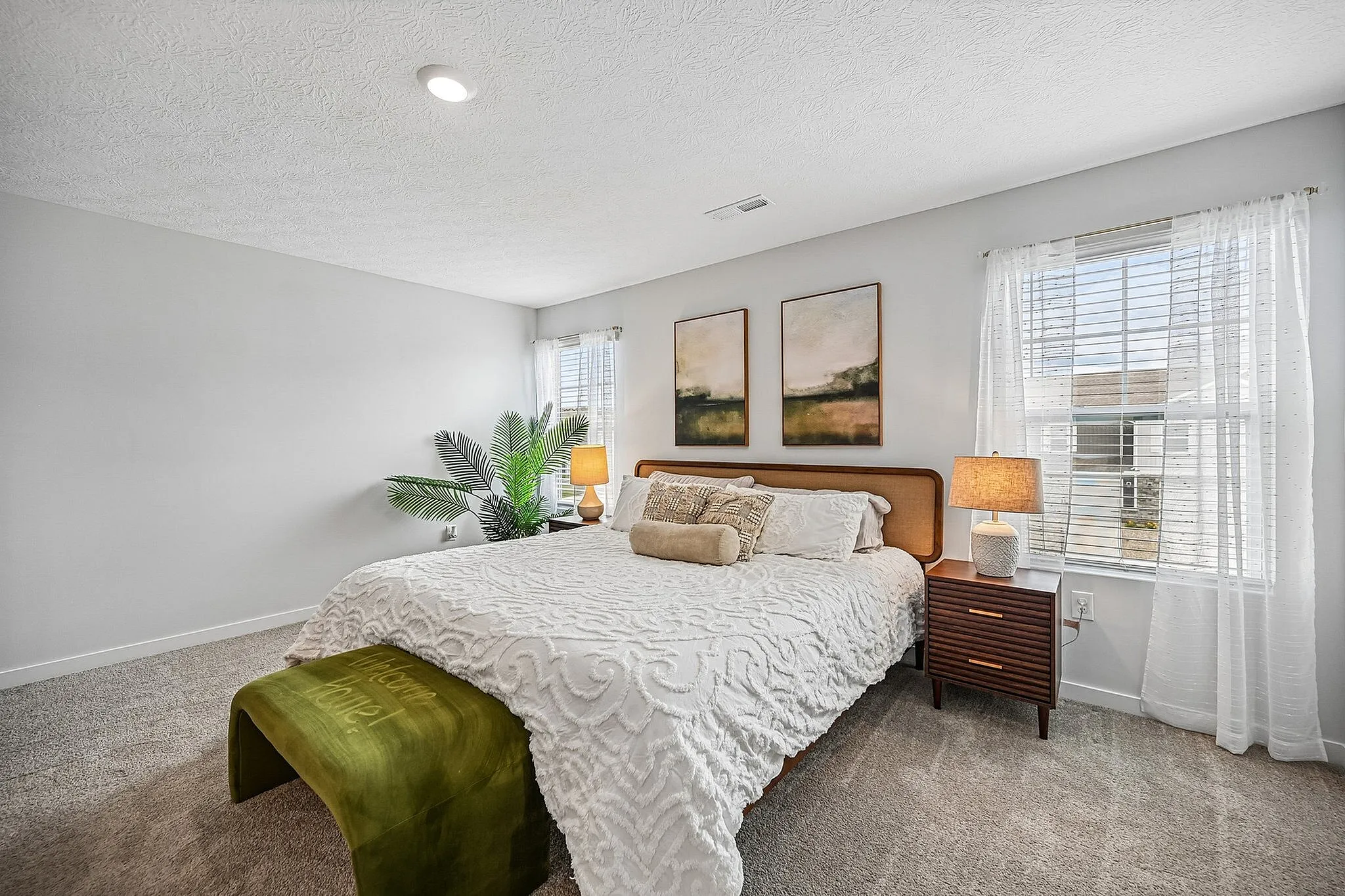 Bright and inviting bedroom with elegant decor, featuring a plush king-size bed, stylish bedside tables, artistic wall art, and ample natural light.