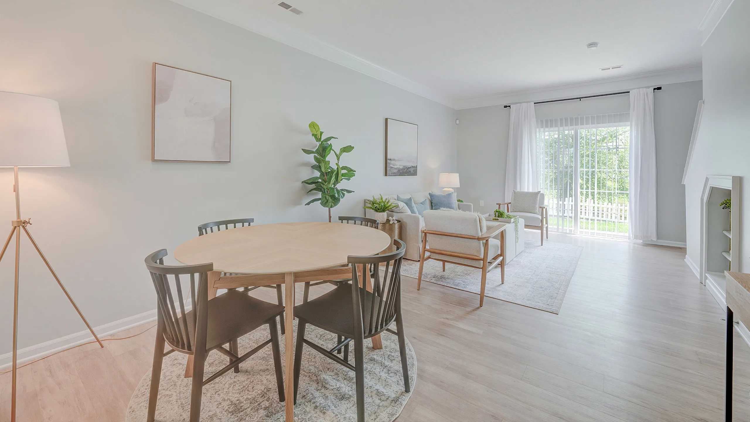 Bright and spacious living area with modern dining set, cozy seating, and large windows overlooking a lush garden.