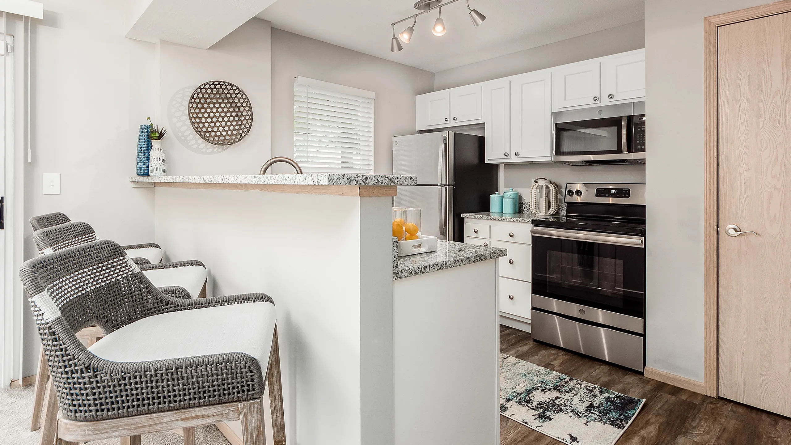 Modern kitchen with sleek stainless steel appliances, chic white cabinets, and a stylish granite countertop bar with wicker stools.