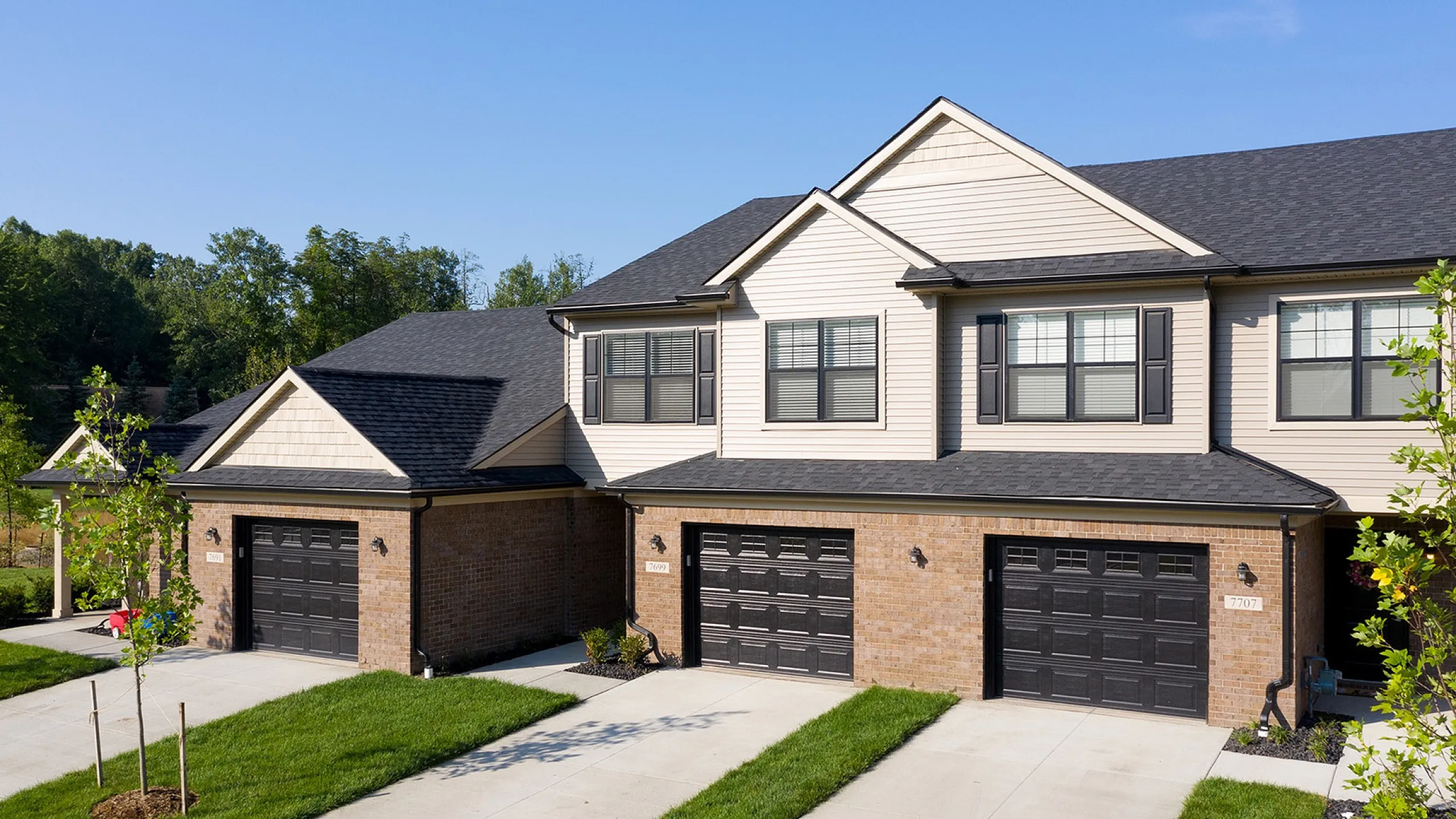 Charming townhouse with elegant brick facade, modern black garage doors, and lush green lawn, ideal for comfortable suburban living.