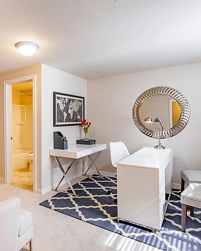 Chic home office with elegant decor, featuring a stylish desk, large mirror, modern artwork, and cozy seating.