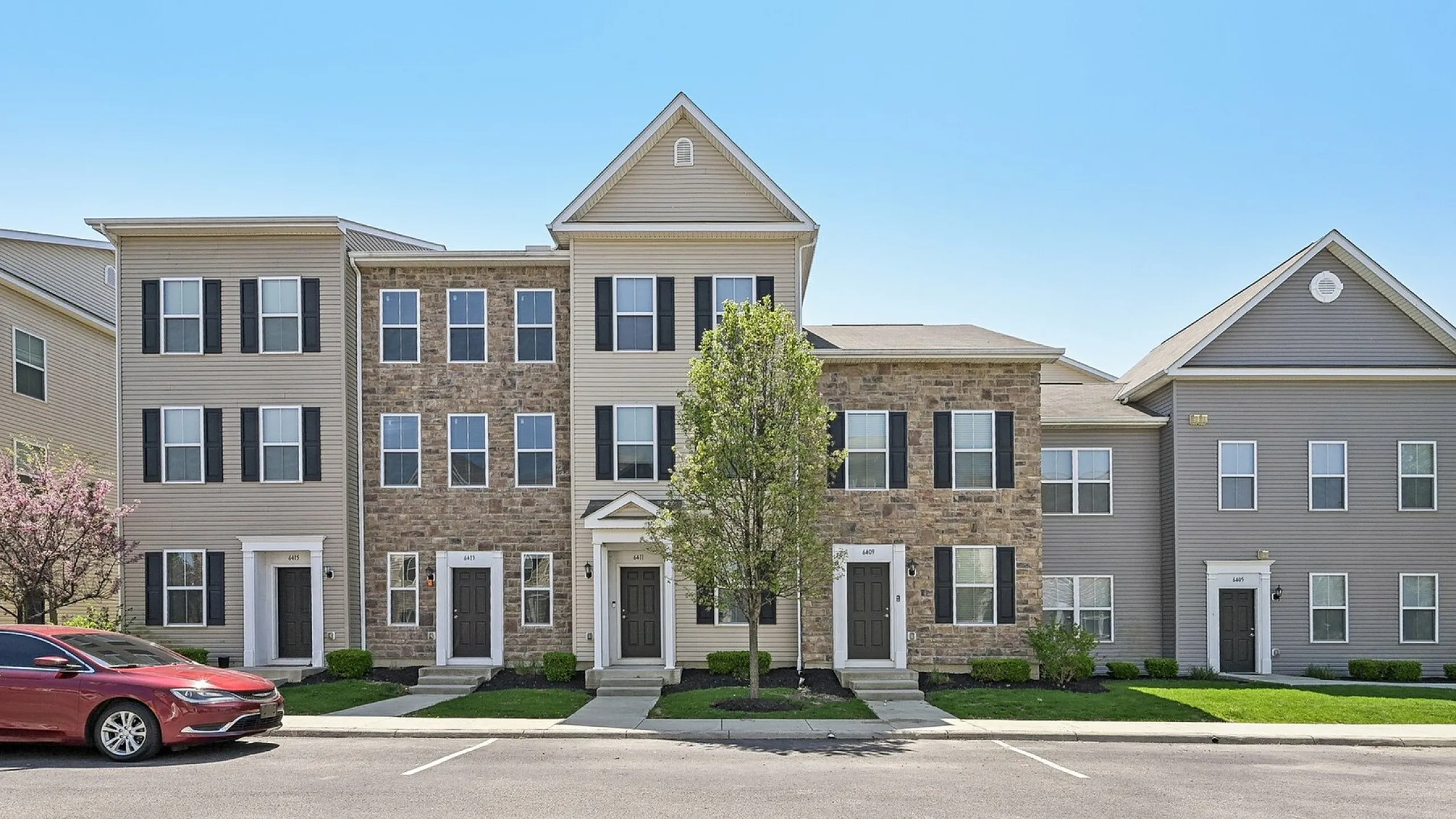 Charming townhouse with brick and siding facade, lush green lawns, and elegant front entrances, perfect for modern living.