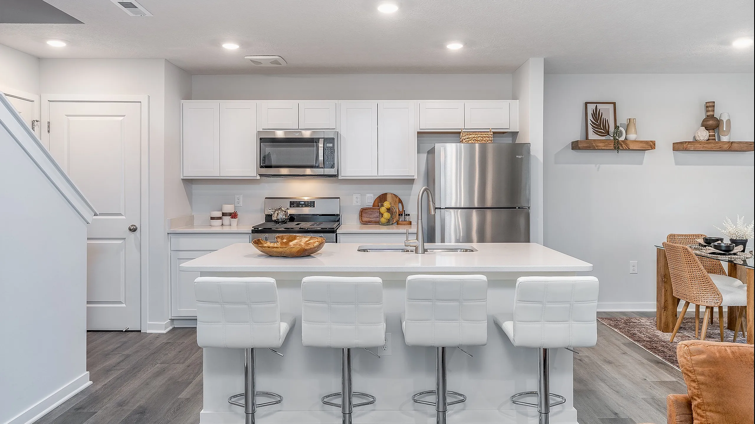 Modern open-plan kitchen with sleek white cabinetry, stainless steel appliances, and a chic island with stylish bar stools.