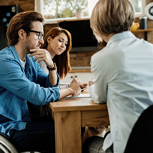 Engaged couple discussing plans at a stylish kitchen table with a friendly advisor, highlighting accessibility and modern interior design.