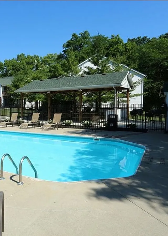 Inviting outdoor pool area featuring comfortable lounge chairs and shaded seating, surrounded by lush greenery and charming residential buildings.
