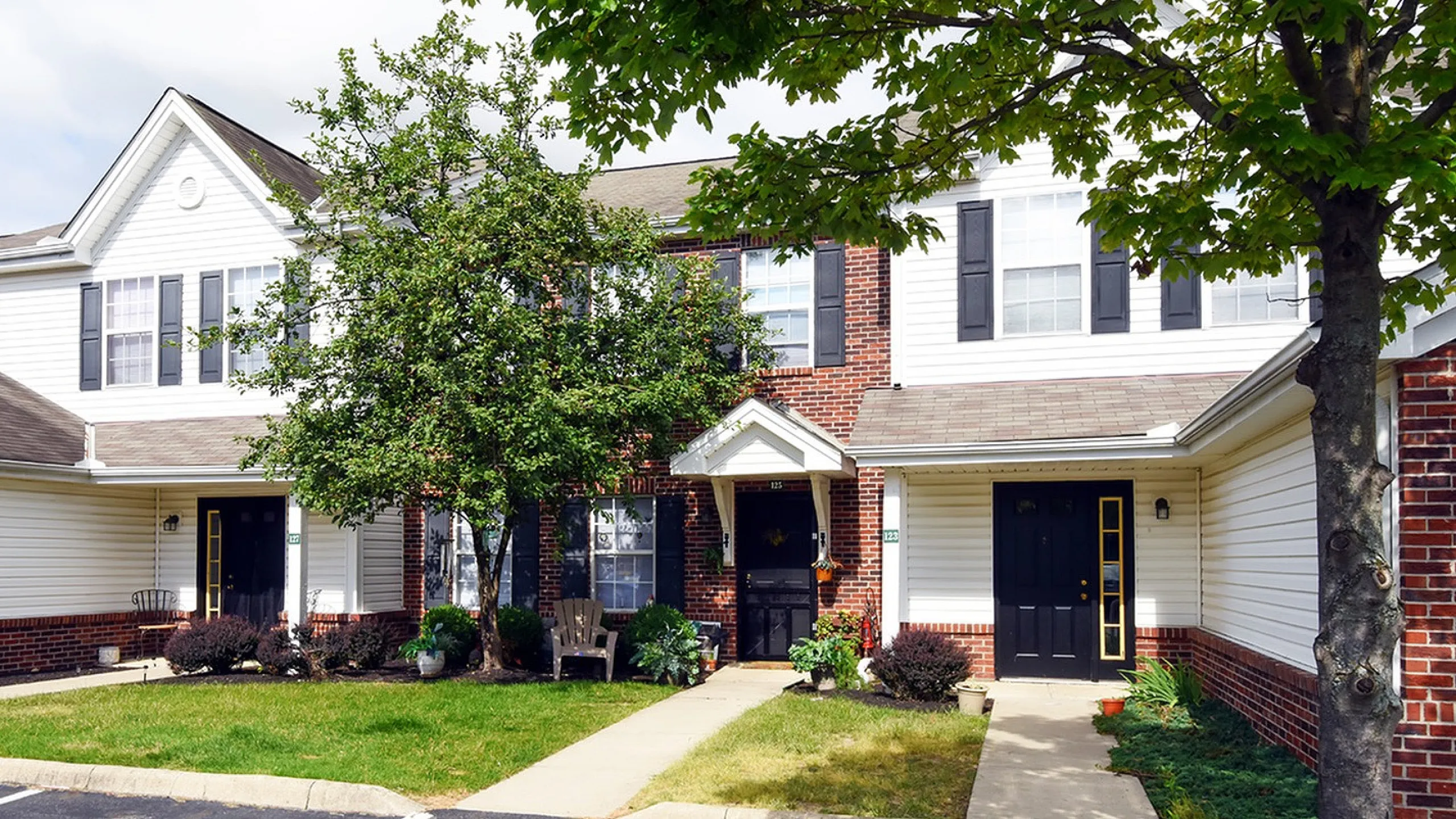 Charming townhouse with brick facade, lush landscaping, and inviting porch in a serene neighborhood.