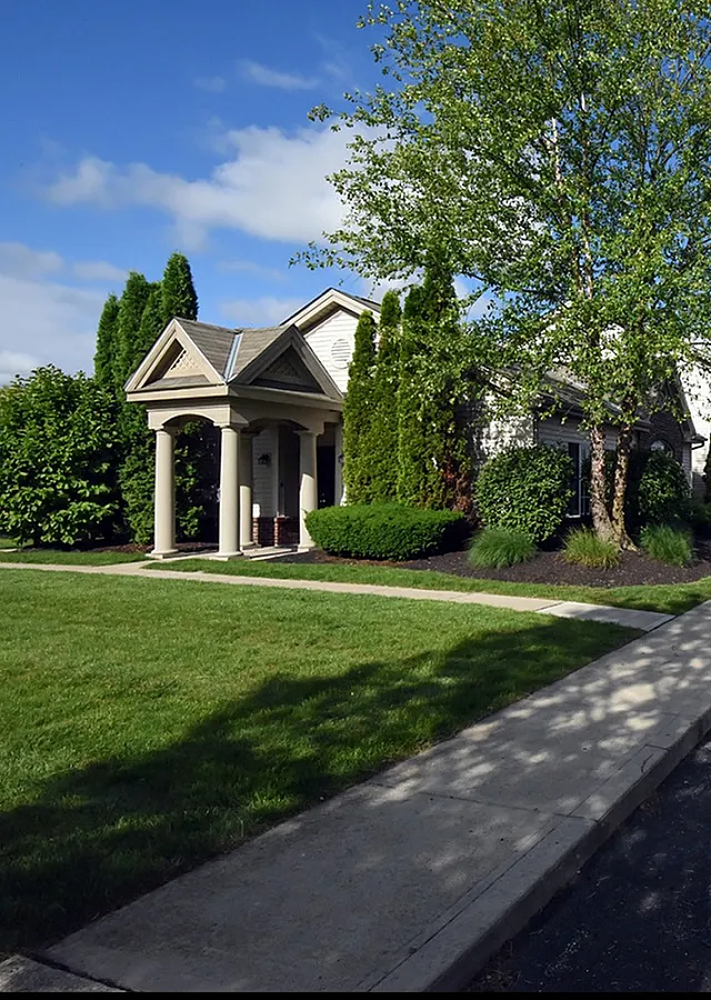 Charming apartment complex with lush landscaping, elegant entrance, and spacious parking area on a sunny day.