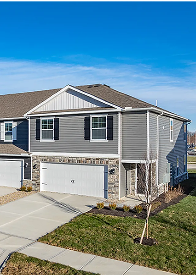 Modern townhouses with elegant grey siding, double garages, and neatly landscaped front yards under a clear blue sky.