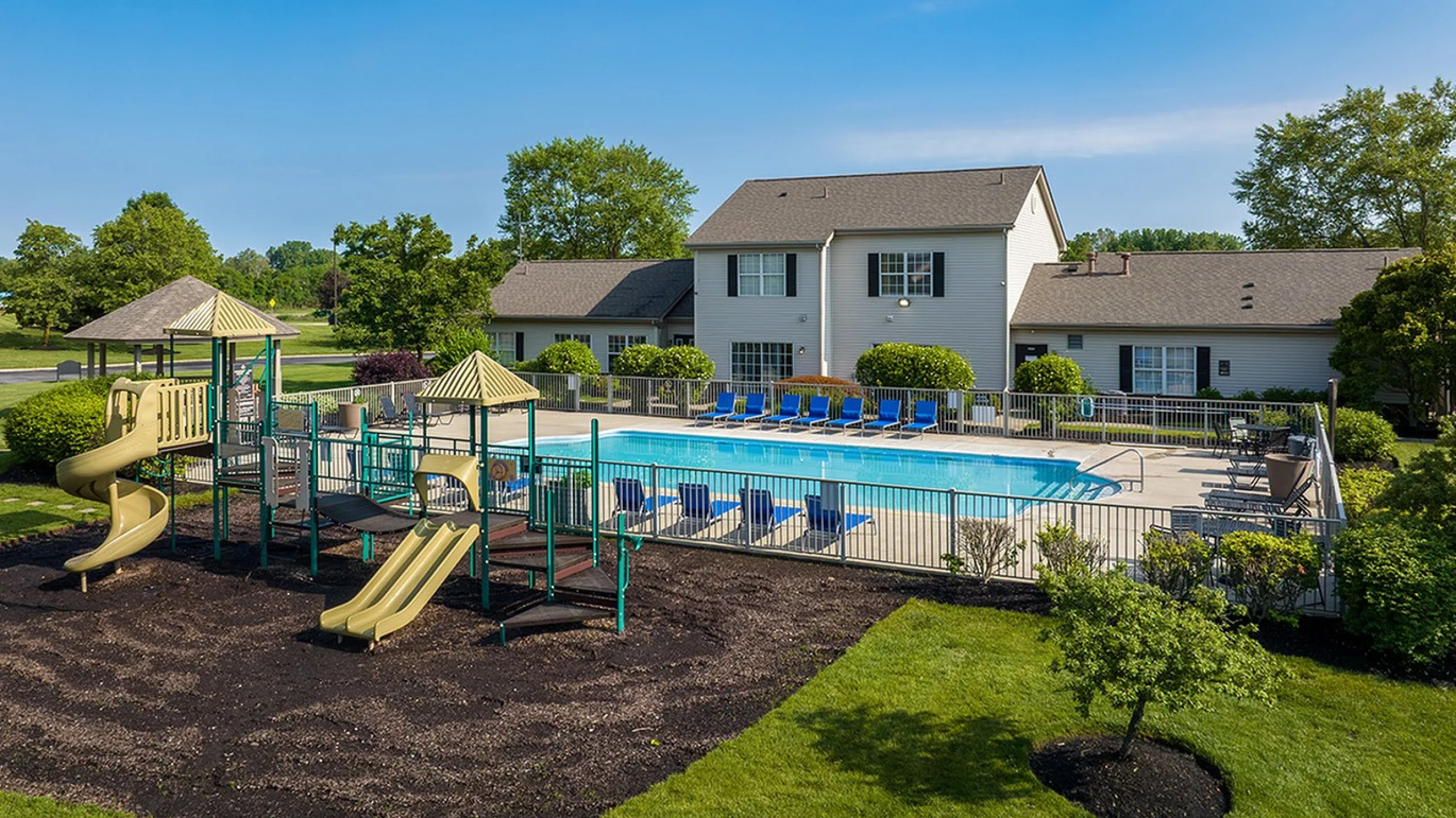 Inviting apartment exterior featuring a refreshing swimming pool and a delightful playground within a lush green setting.